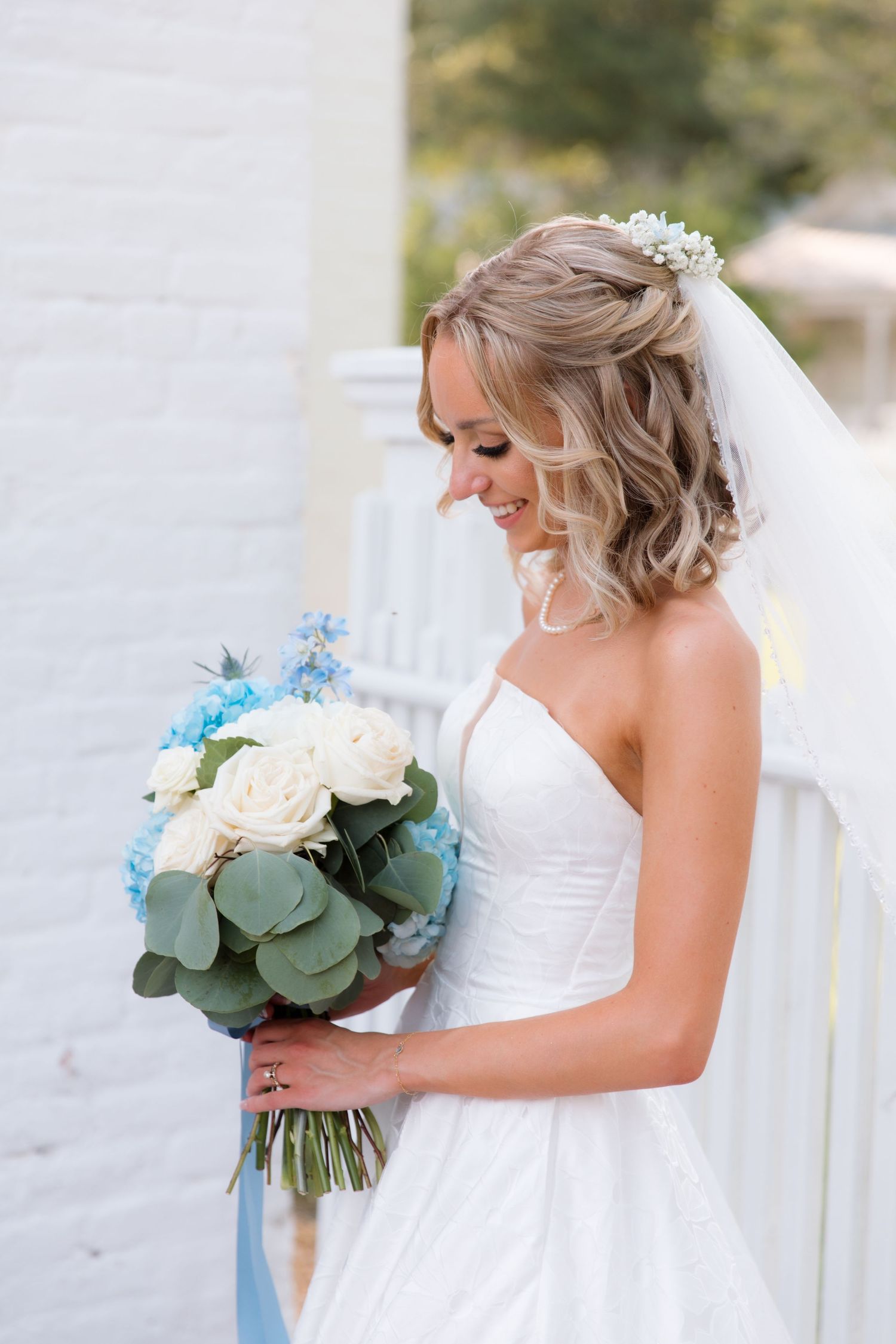 Bride with wavy hair looks down at bouquet featuring eucalyptus and blue florals.