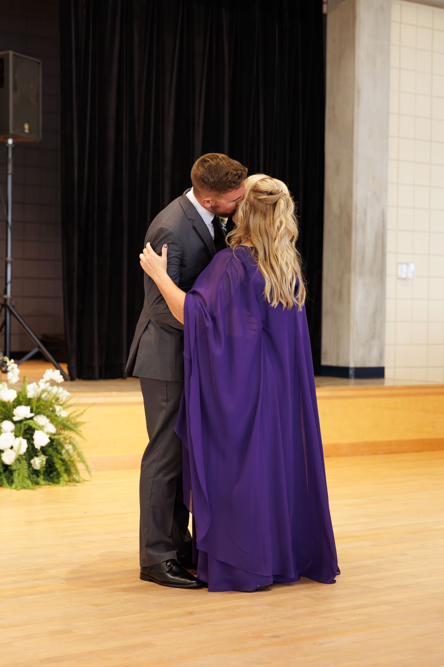 Wedding dance embrace with purple-robed guest in reception hall.