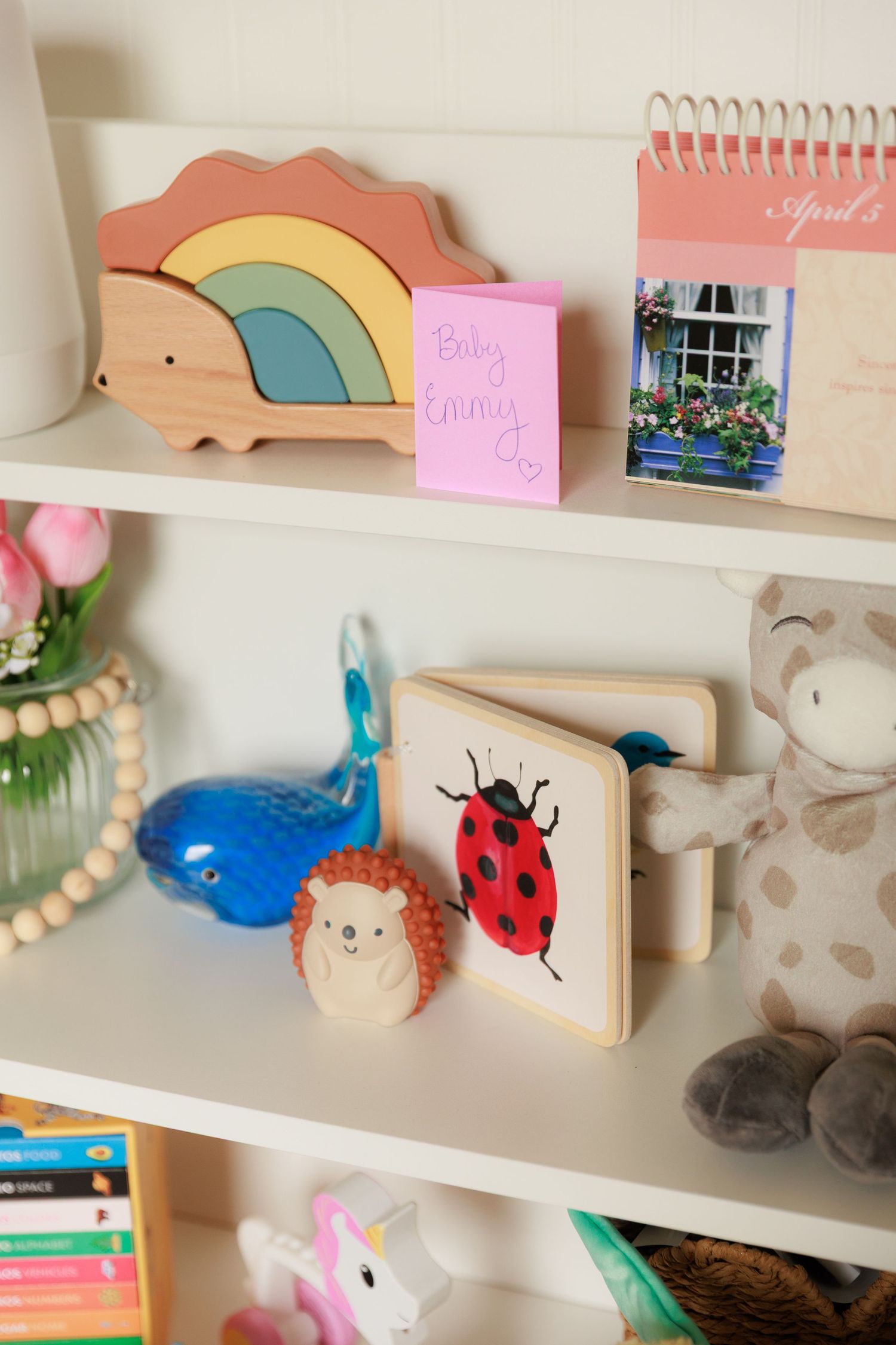 Colorful children's shelf displaying wooden toys, rainbow decor, plush animals, books and decorative items on white shelves.
