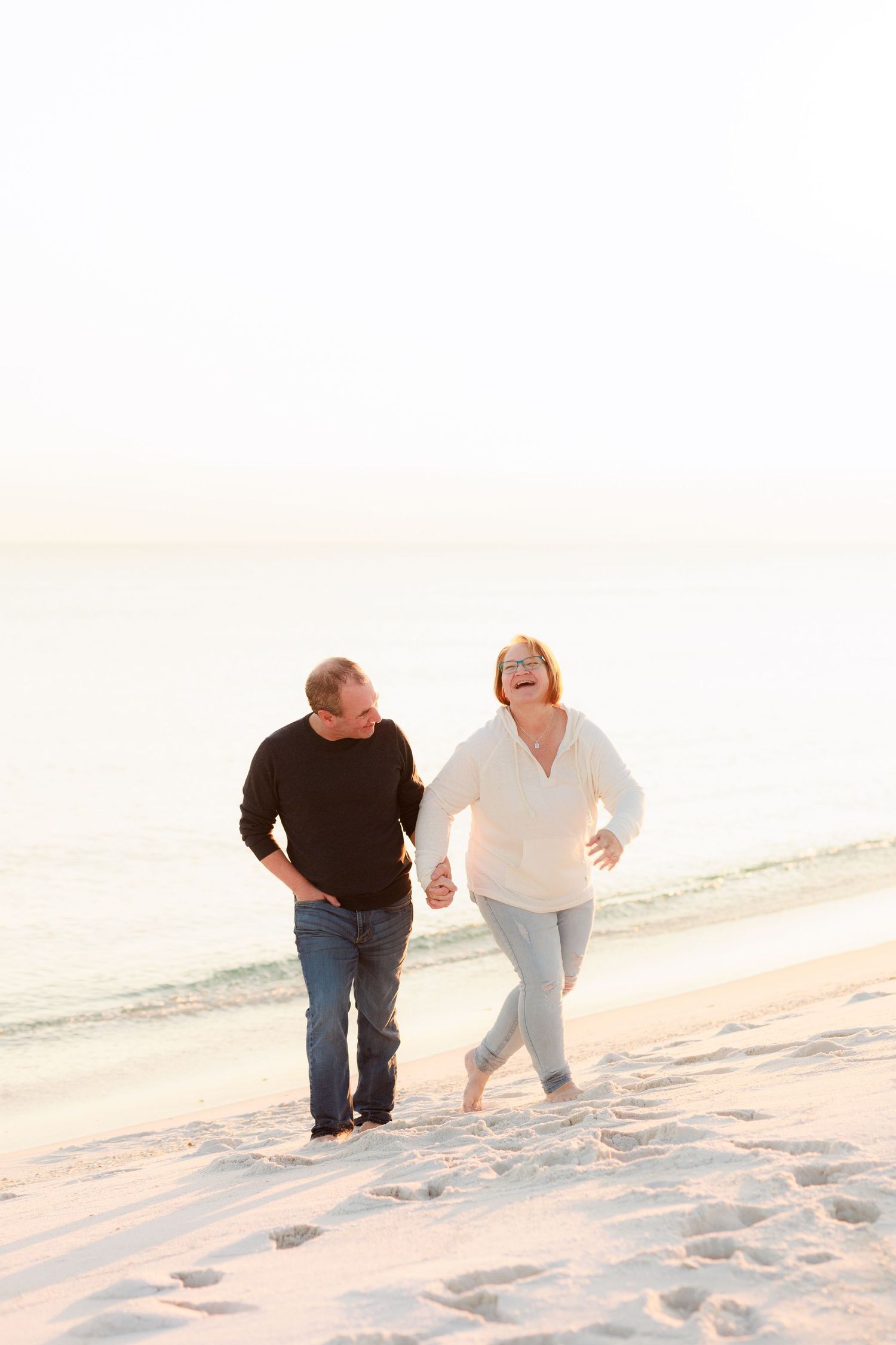 Couple playfully running and laughing together on a sandy beach at sunset.