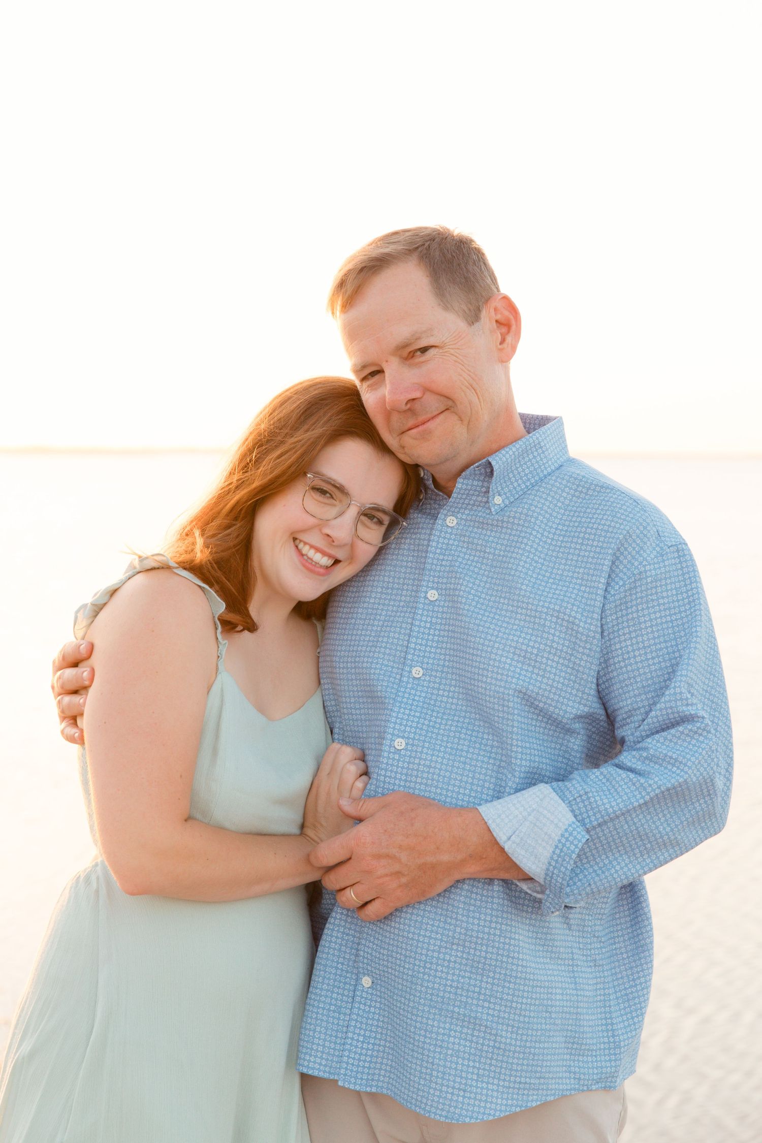 Couple embraces tenderly on beach boardwalk wearing coordinated blue and mint colored outfits.
