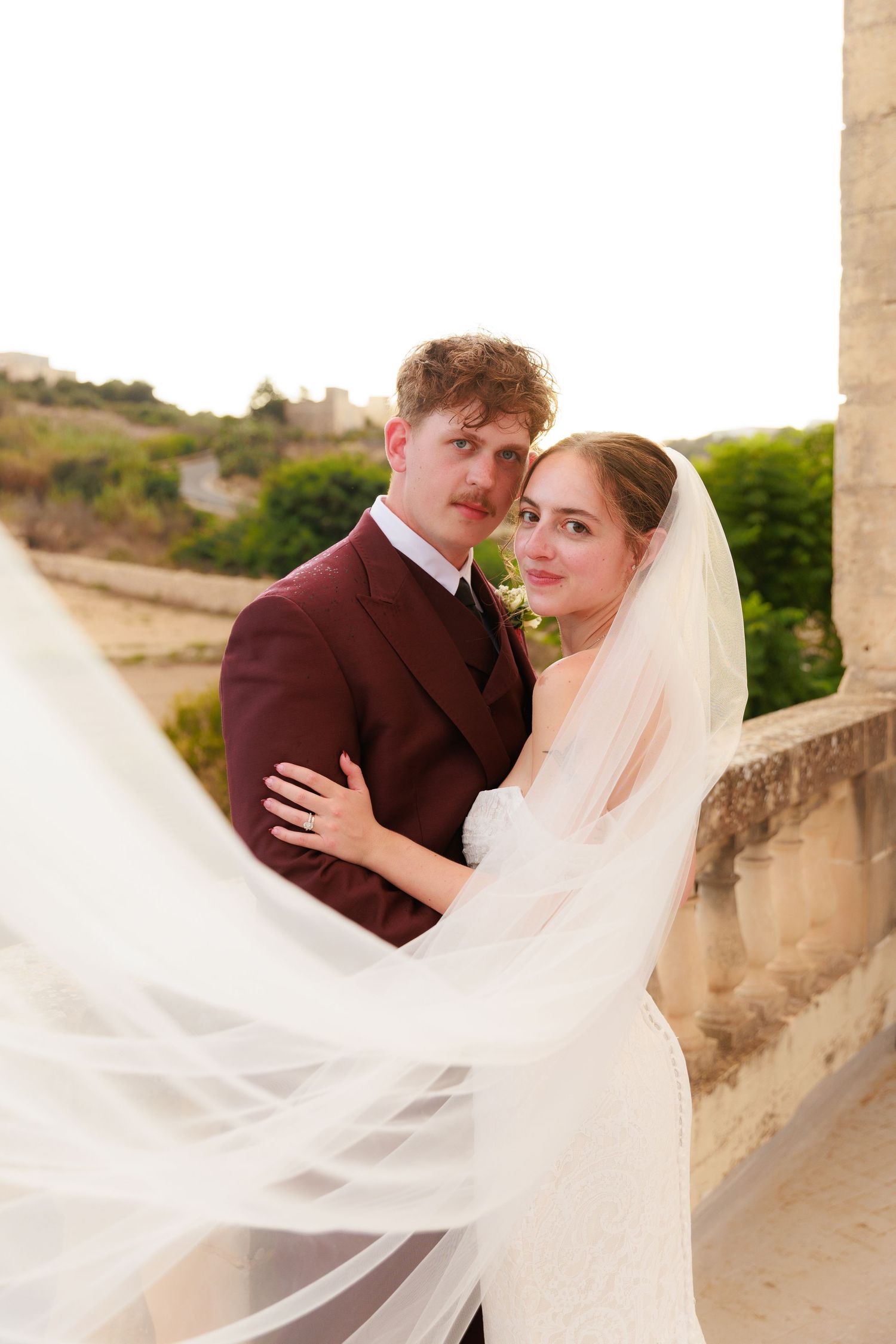 A romantic wedding photo featuring a flowing veil catching the breeze on a scenic stone terrace.