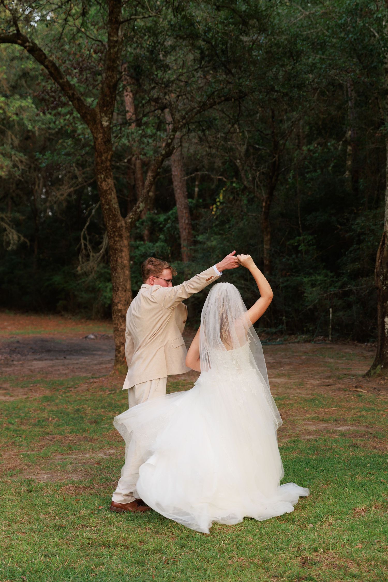 A couple dancing together outdoors, with the bride's white dress flowing as they twirl in a wooded setting.