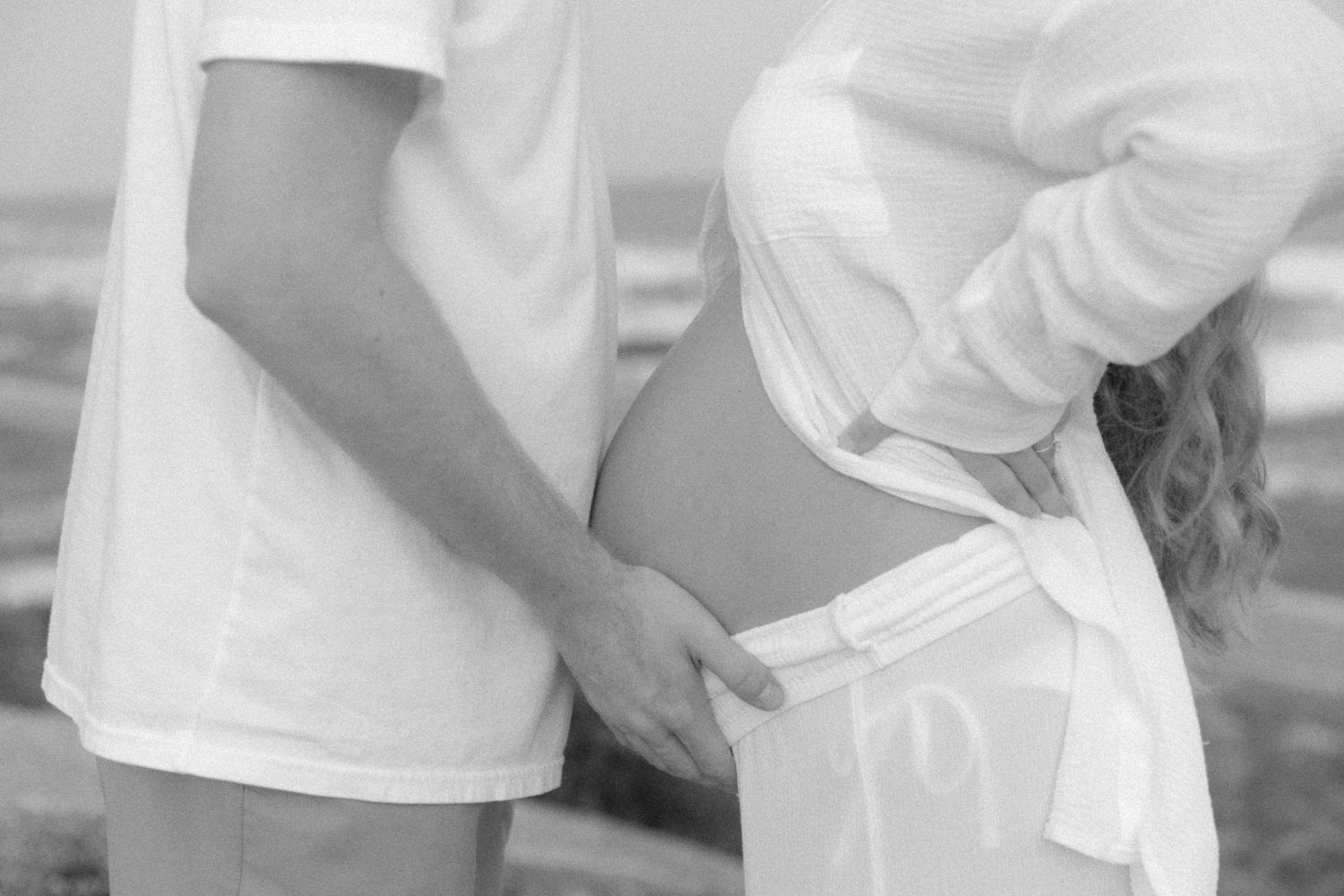Close-up detail shot of hands tenderly embracing a pregnant belly.
