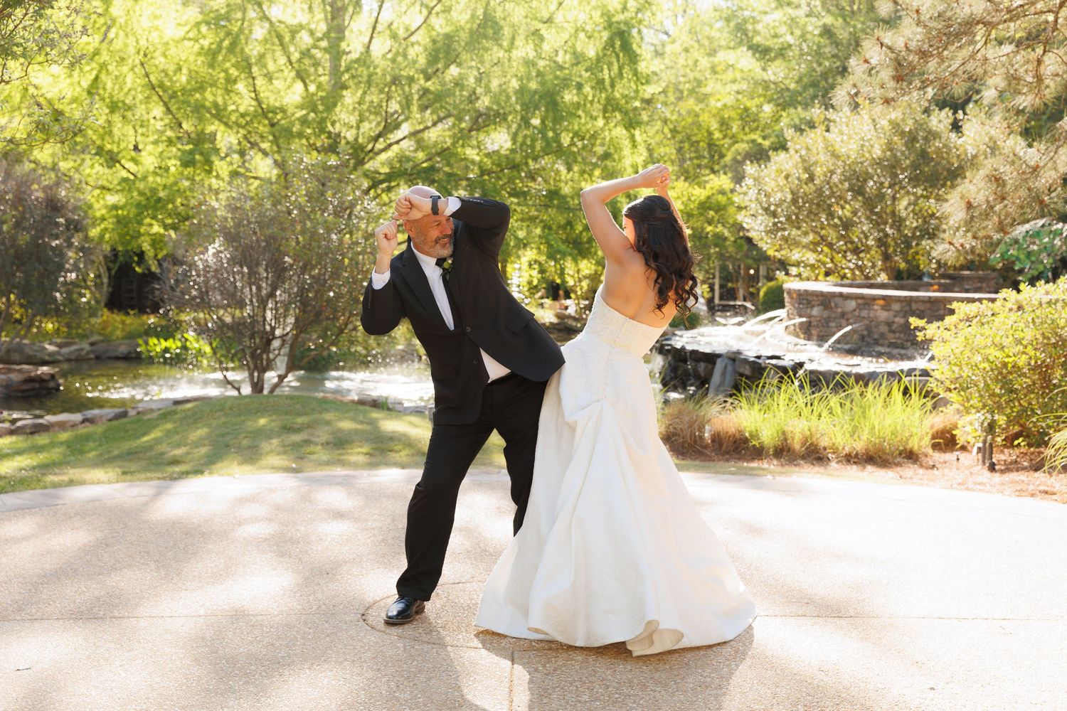 Bride and groom dancing joyfully outdoors, with the groom dipping the bride in a white wedding gown.