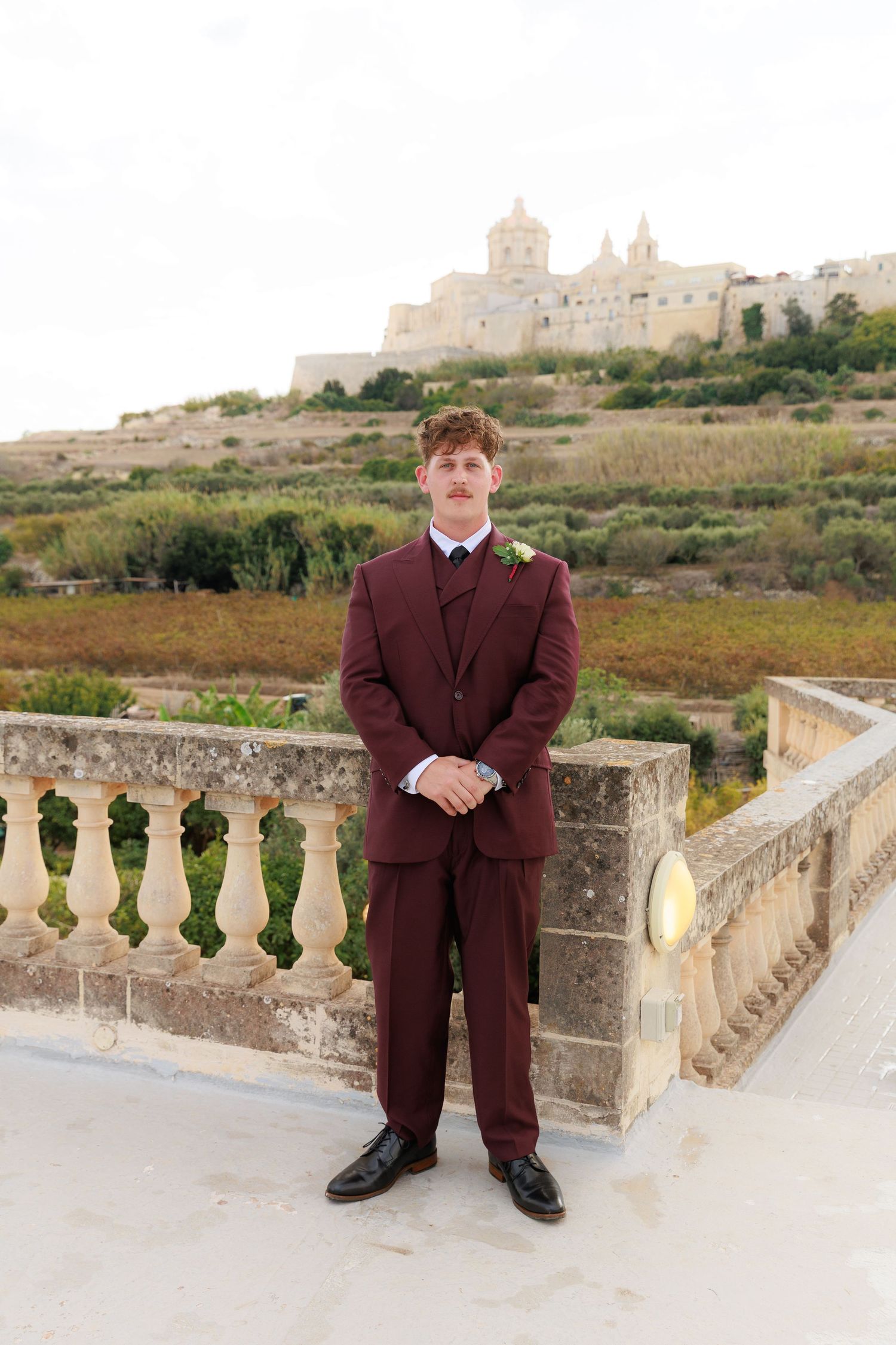 A series of photos showing someone in a brown suit posing on a stone balcony with a historic building in the background.