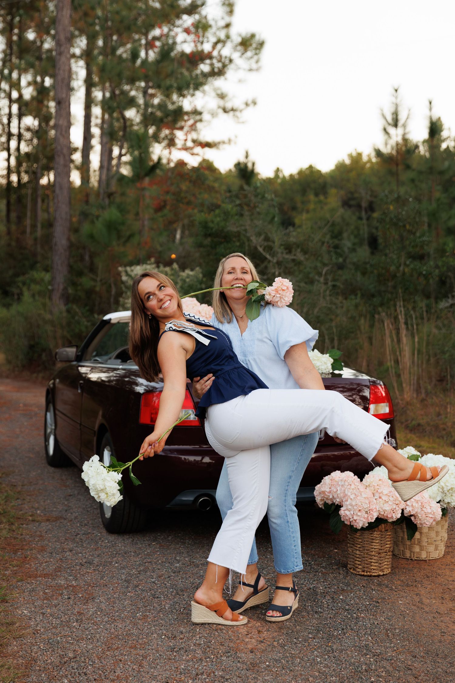 A romantic picnic scene with a couple in casual attire posing playfully near a vintage car at sunset.