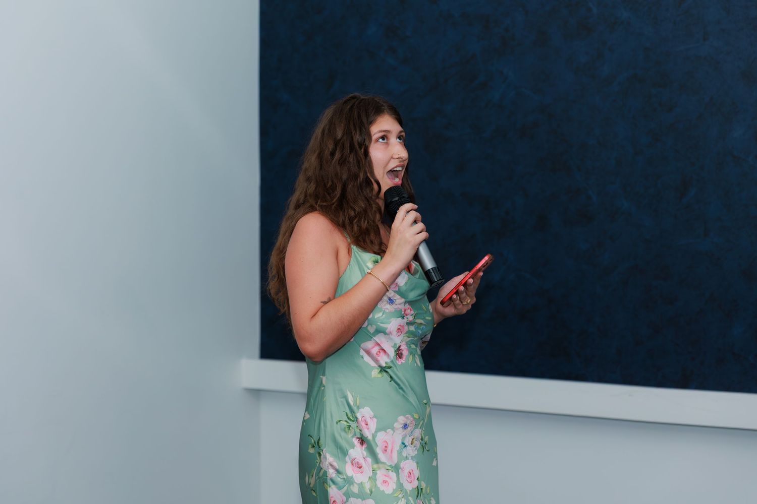 Someone in green dress gestures while presenting with a whiteboard in the background during a meeting.