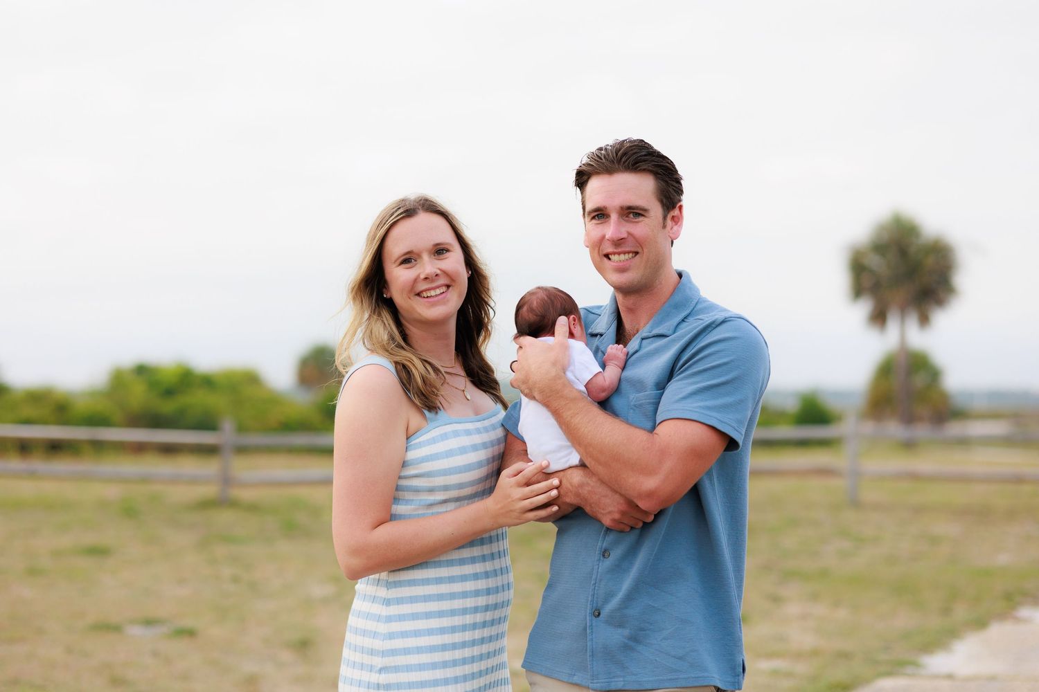 A couple stands together in an outdoor setting holding their small dog while sharing tender moments in nature.