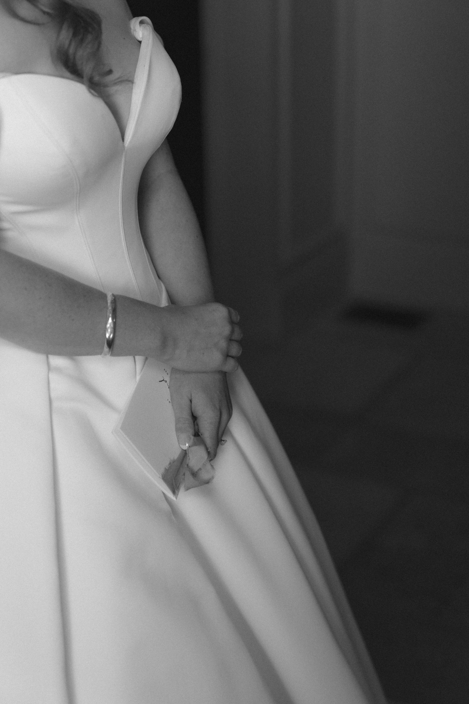 Black and white photo of a bride in a strapless ball gown wedding dress, hands clasped holding a note.