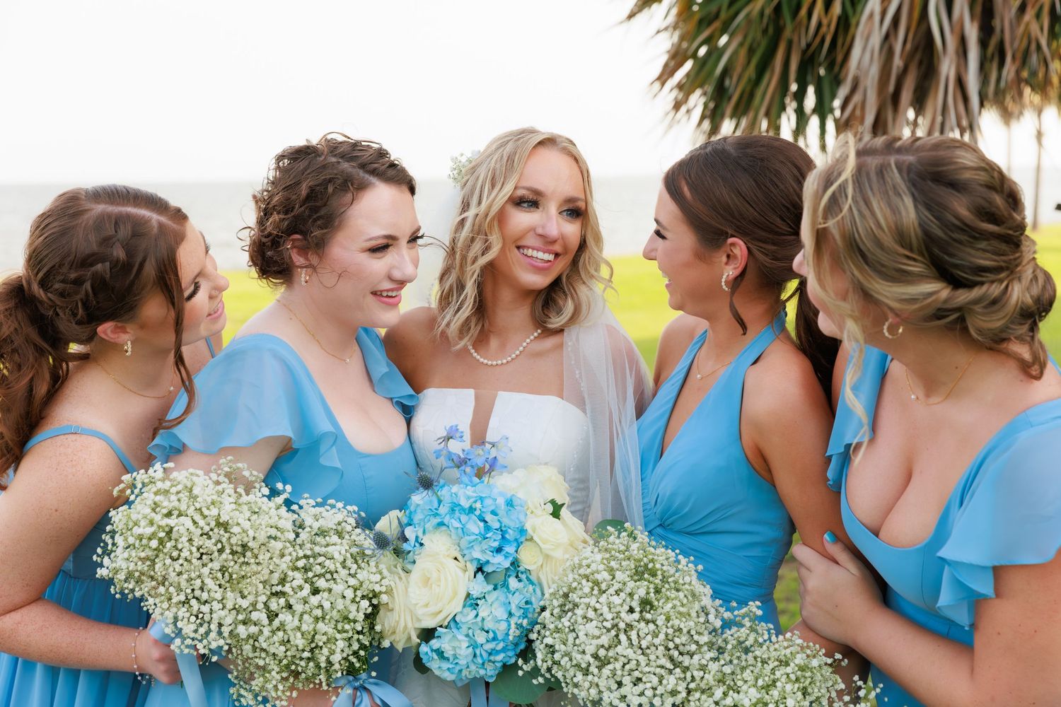 Wedding party gathers for closeup photo with white and blue floral bouquets.
