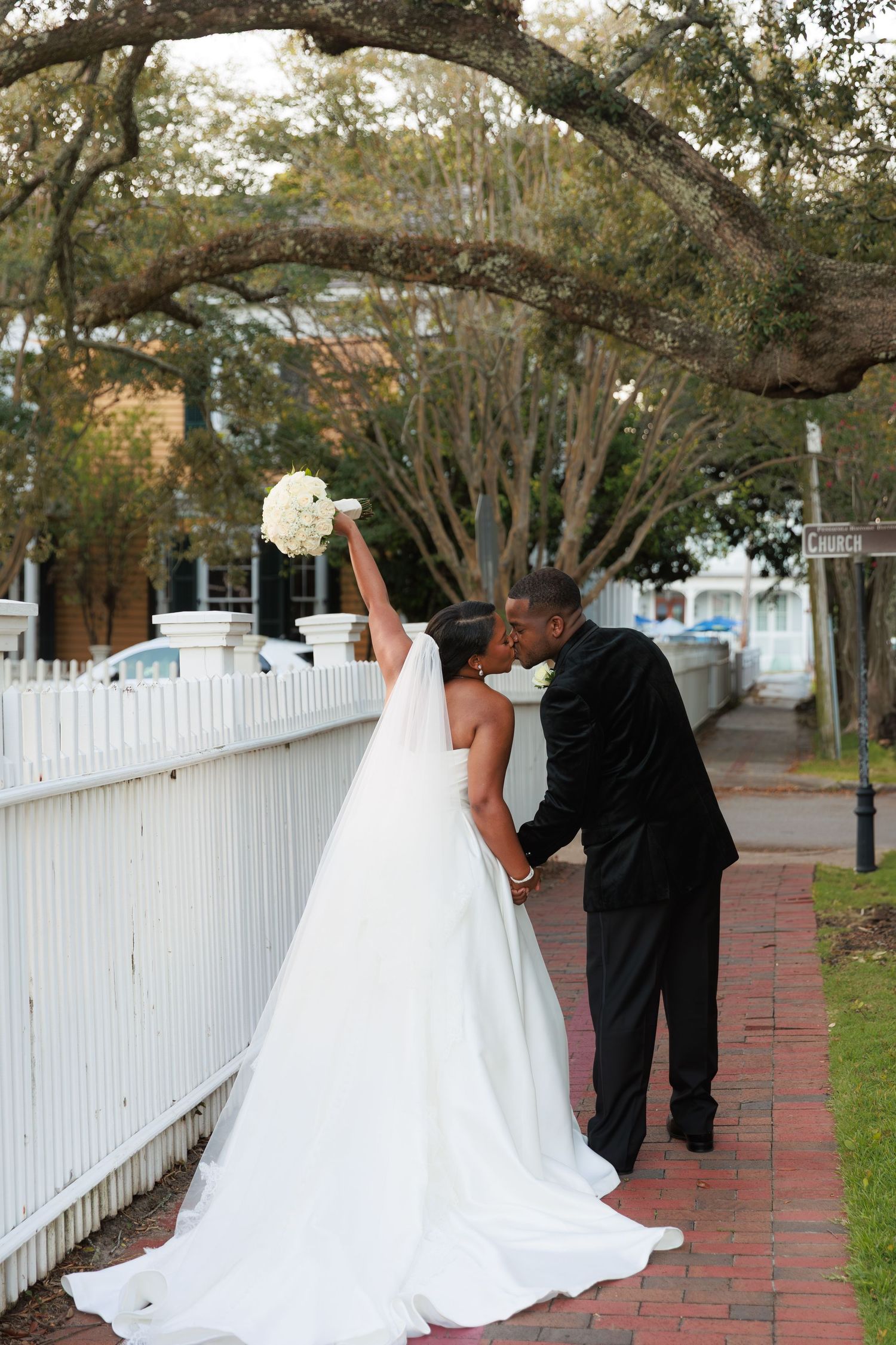 A romantic wedding couple shares intimate moments along a white picket fence walkway.
