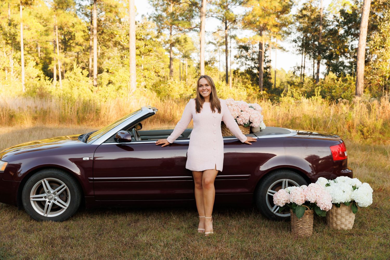 A burgundy vintage convertible car parked in a golden autumn forest setting during a photo session.