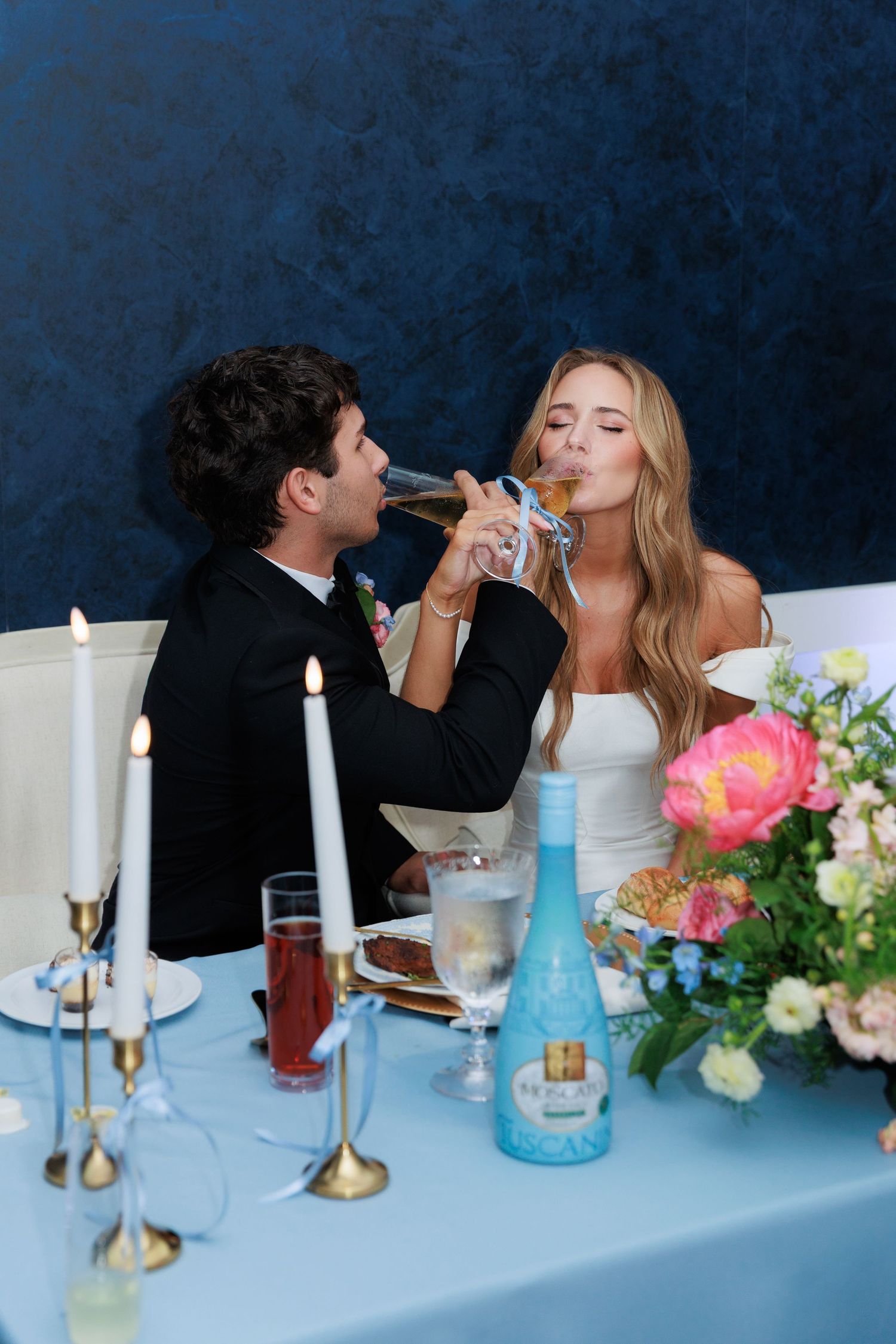 A couple shares a romantic moment at an elegant dinner table set with blue tablecloth, candles and floral decorations.
