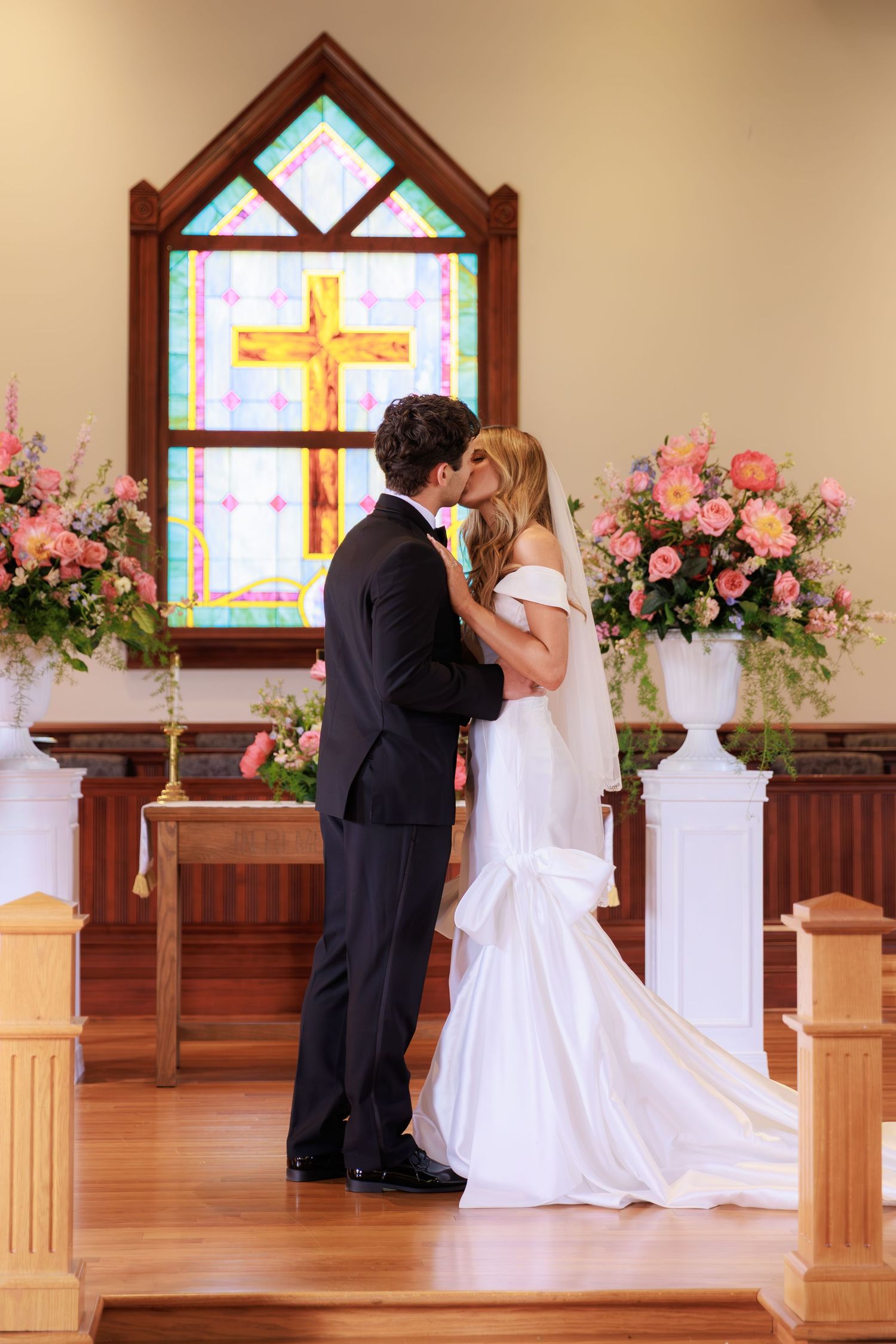 Romantic wedding ceremony moment in front of stained glass windows and pink floral decorations.