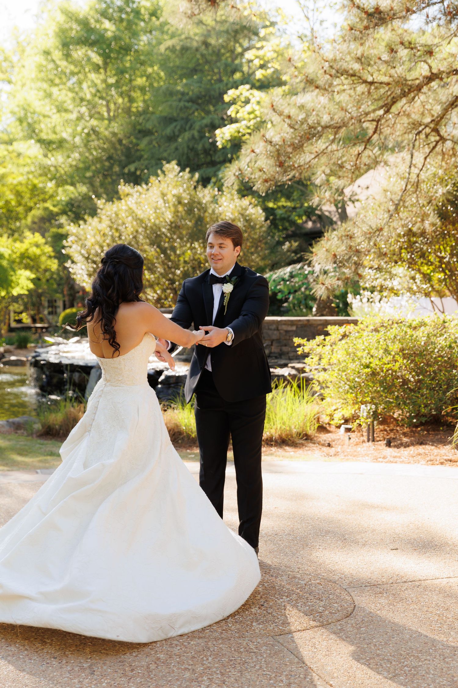 Bride and groom holding hands outdoors in a lush garden setting, sharing a romantic first look moment.