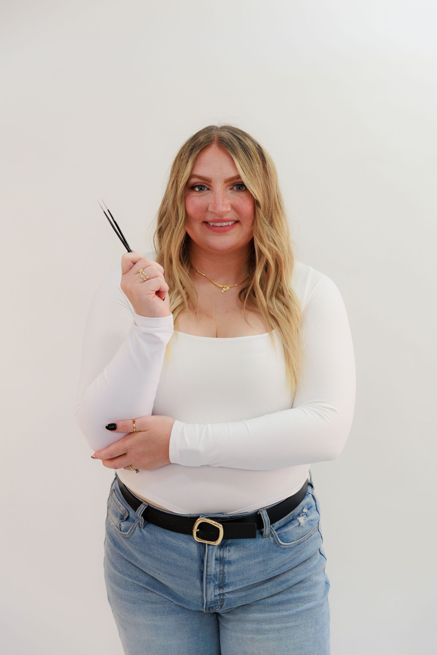 Casual portrait holding lash styling tools against white background.