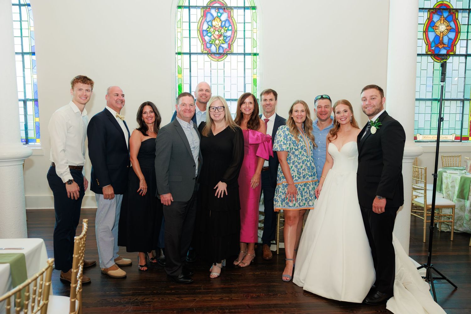 Group of family and friends posing with bride and groom inside a chapel with stained glass windows.