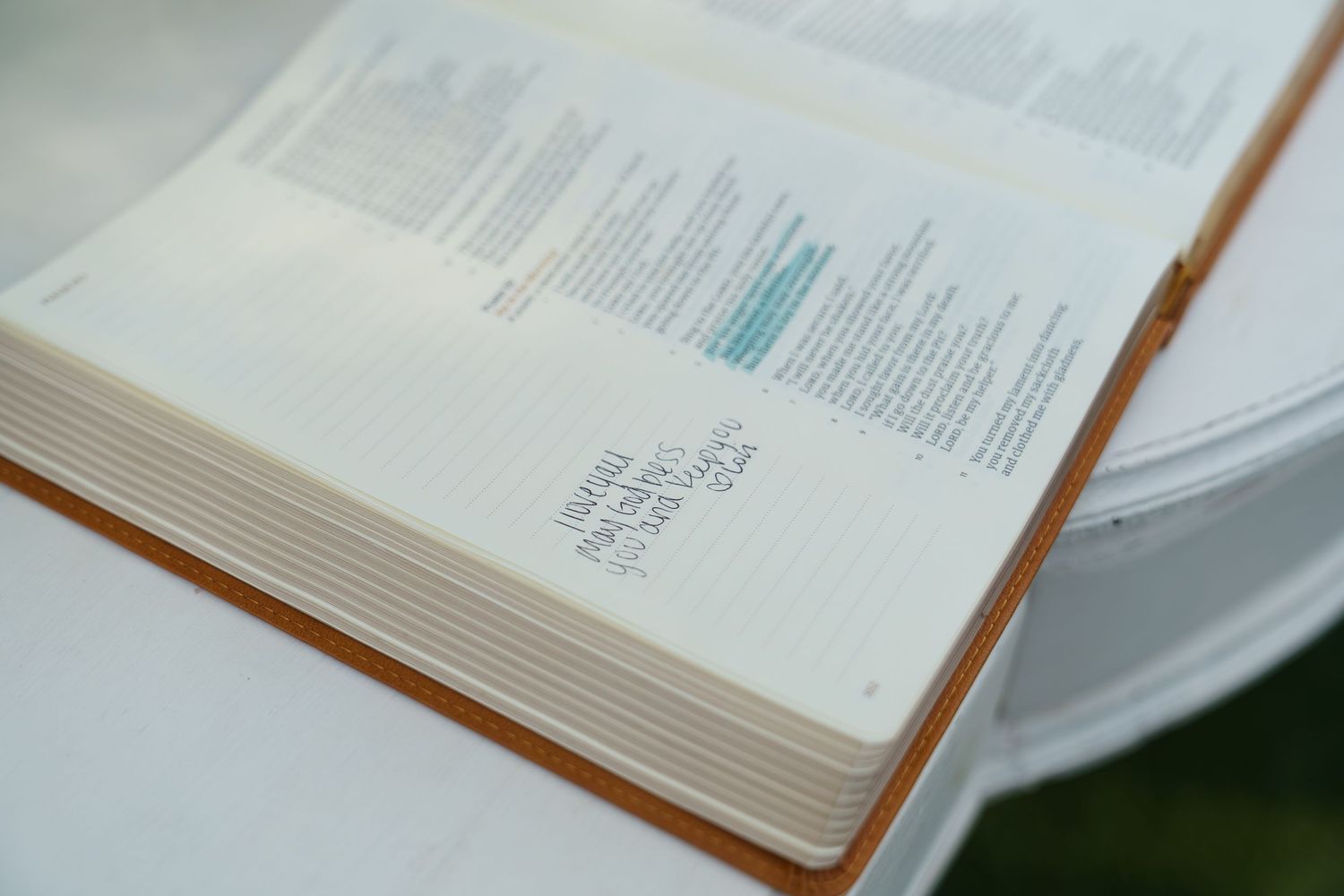 Open hardcover journal with lined pages and teal text resting on a white surface outdoors.