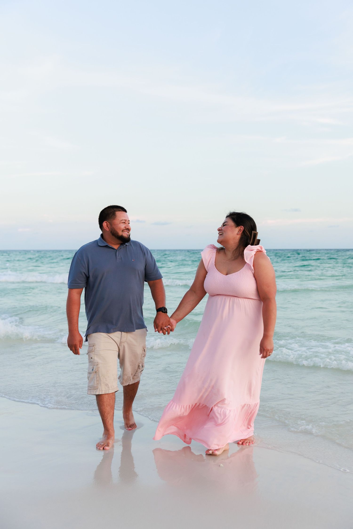 A couple walks hand in hand along a beach at sunset, with turquoise waters and white sand beneath their feet.