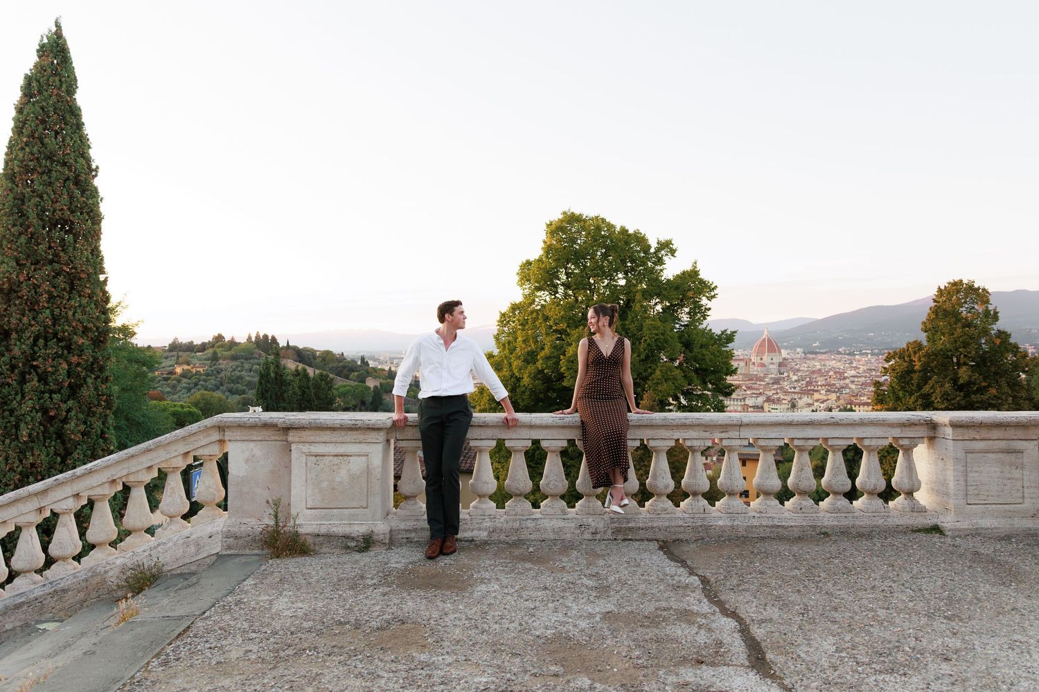 Couple holding hands on a stone terrace overlooking Florence skyline at sunset.
