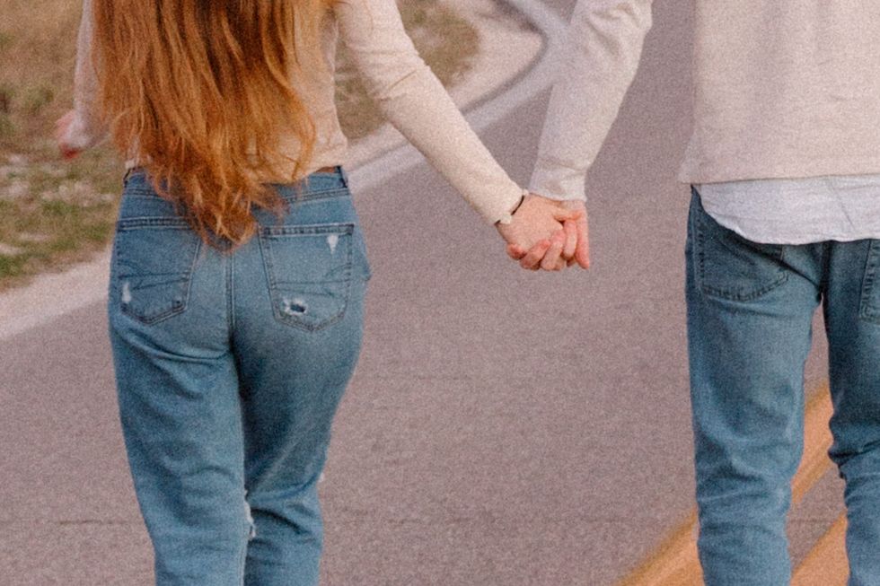 A person in blue jeans and brown boots walks along a paved path on an autumn day.