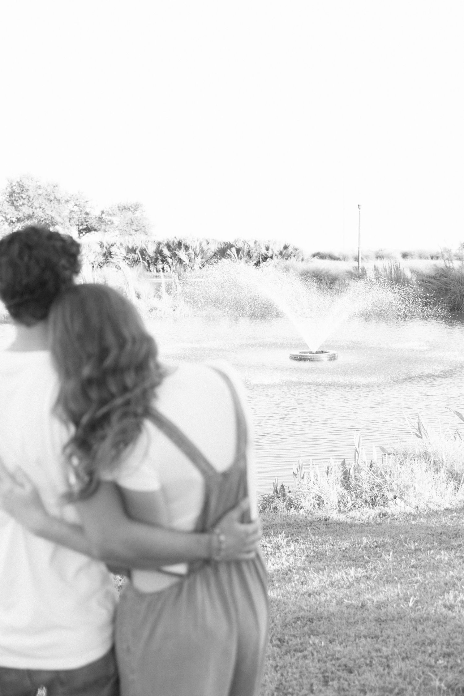 A black and white series of photos showing two people walking together with their arms around each other by a lake.