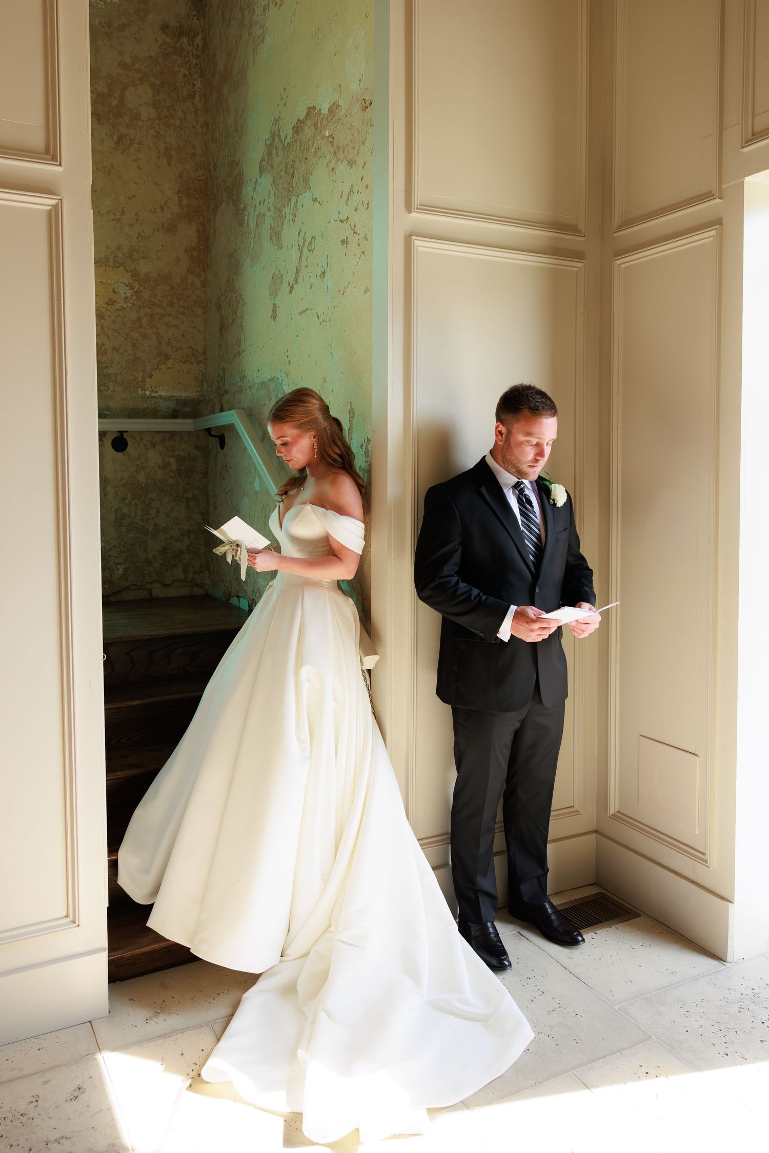 Bride and groom reading letters before wedding ceremony, standing on opposite sides of a doorway in elegant venue.