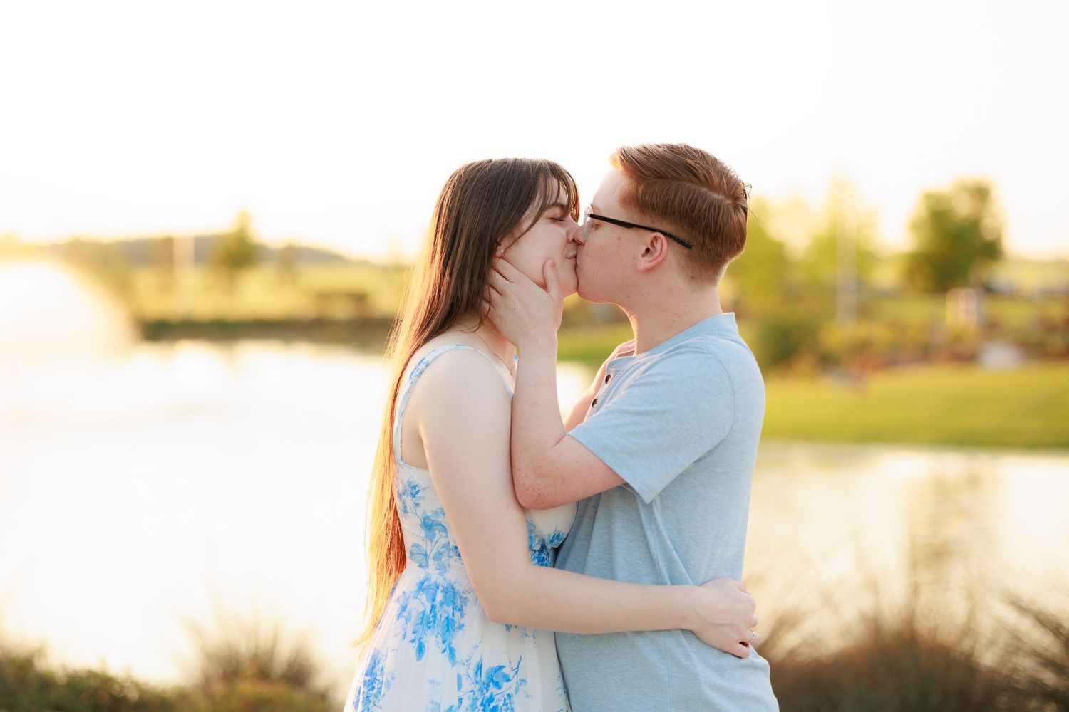 Couple sharing a romantic kiss outdoors near a lake during golden hour sunset.