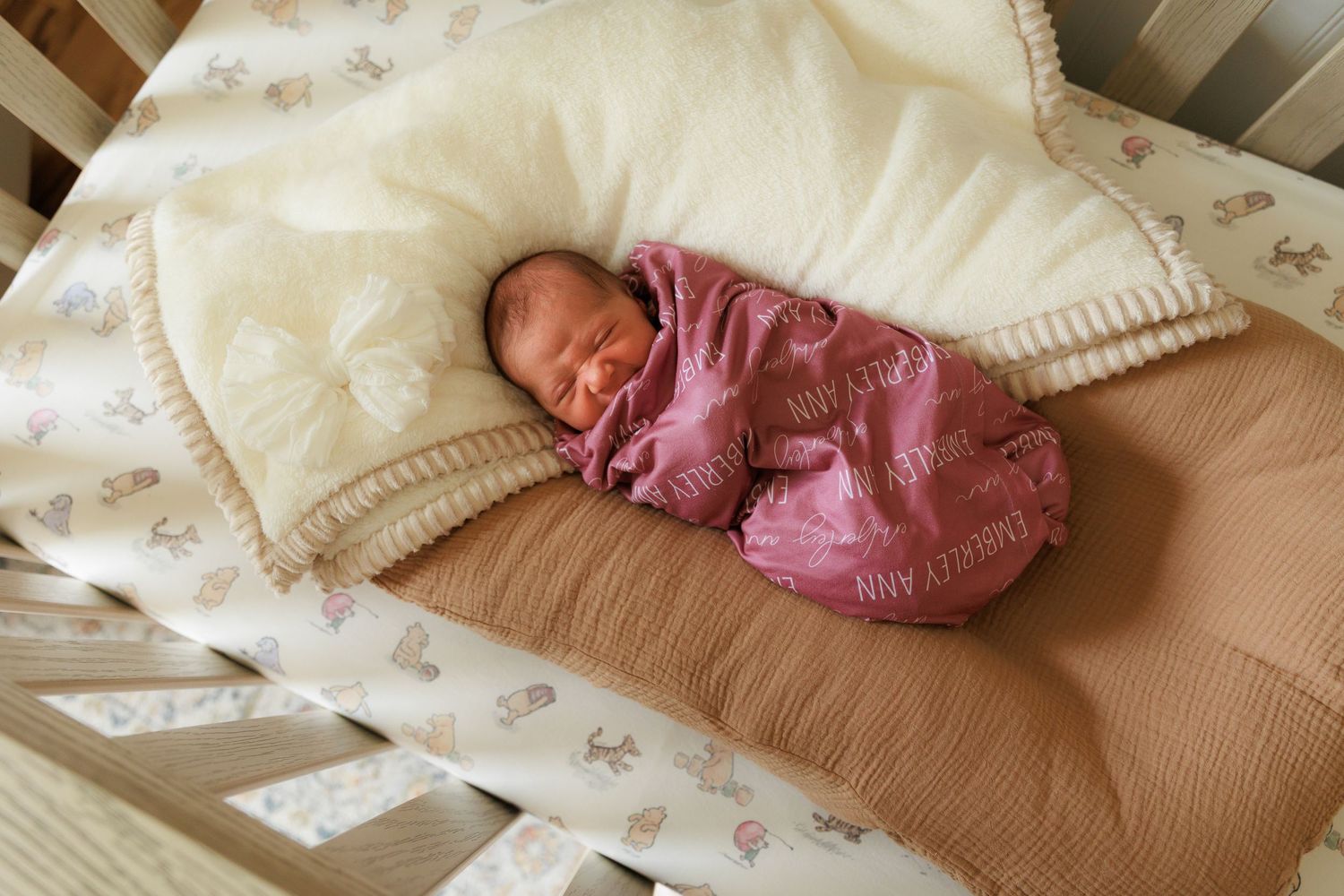 A sleeping baby in pink clothing rests peacefully on a beige blanket with white trim.