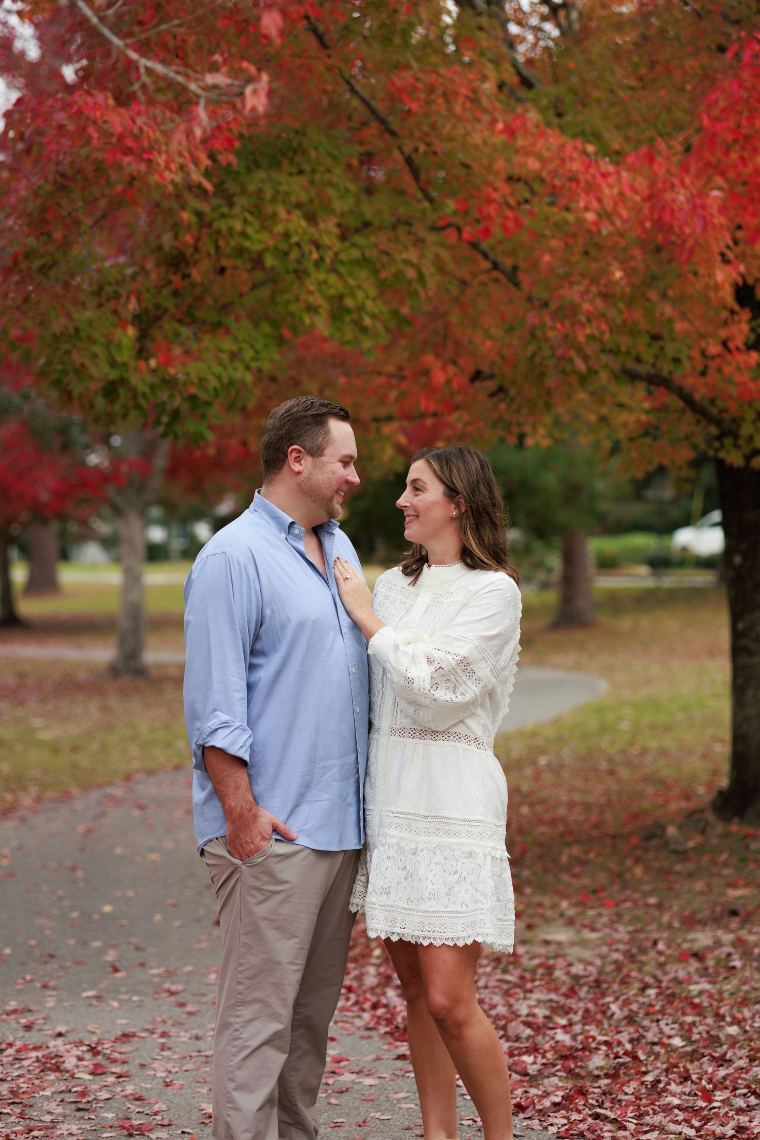 A couple shares a romantic moment under vibrant red fall foliage in a park setting.