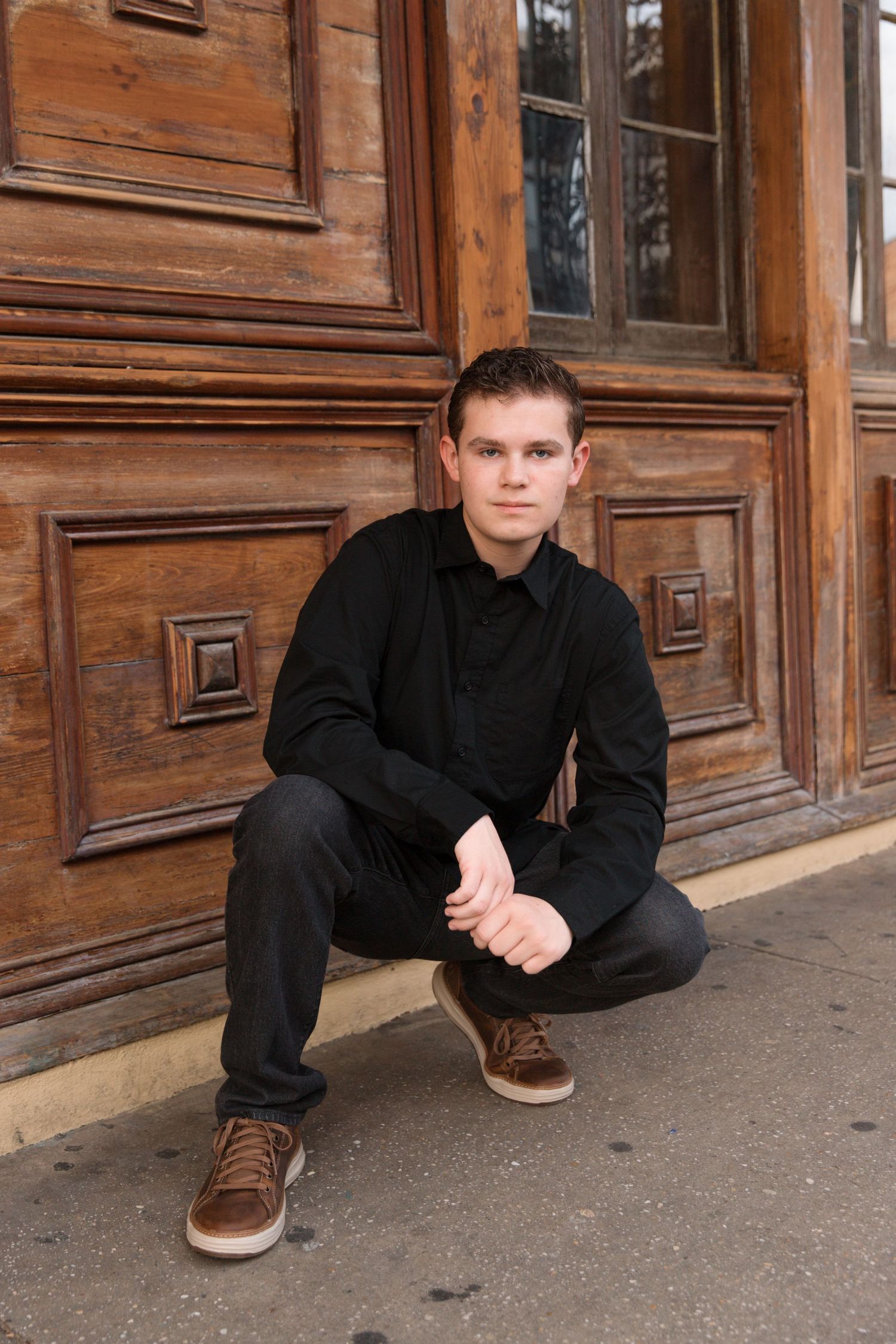 Person in black clothing crouches beside decorative wooden door.