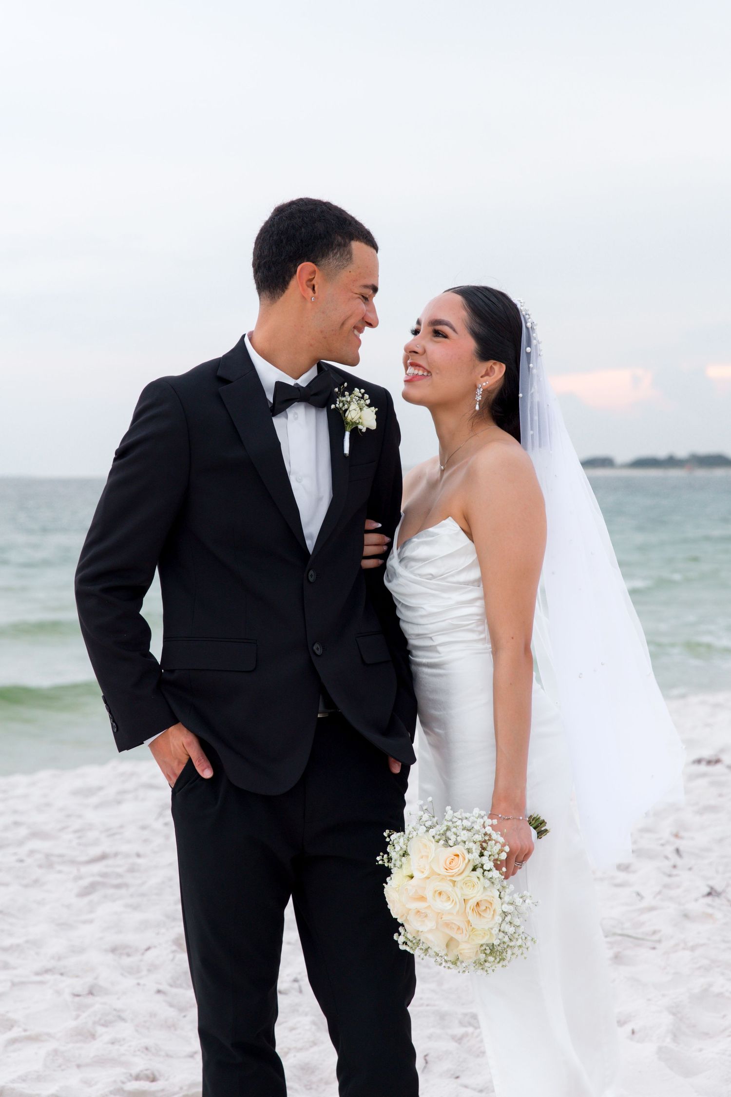 Elegant beach wedding portrait with couple in formal attire against ocean backdrop.