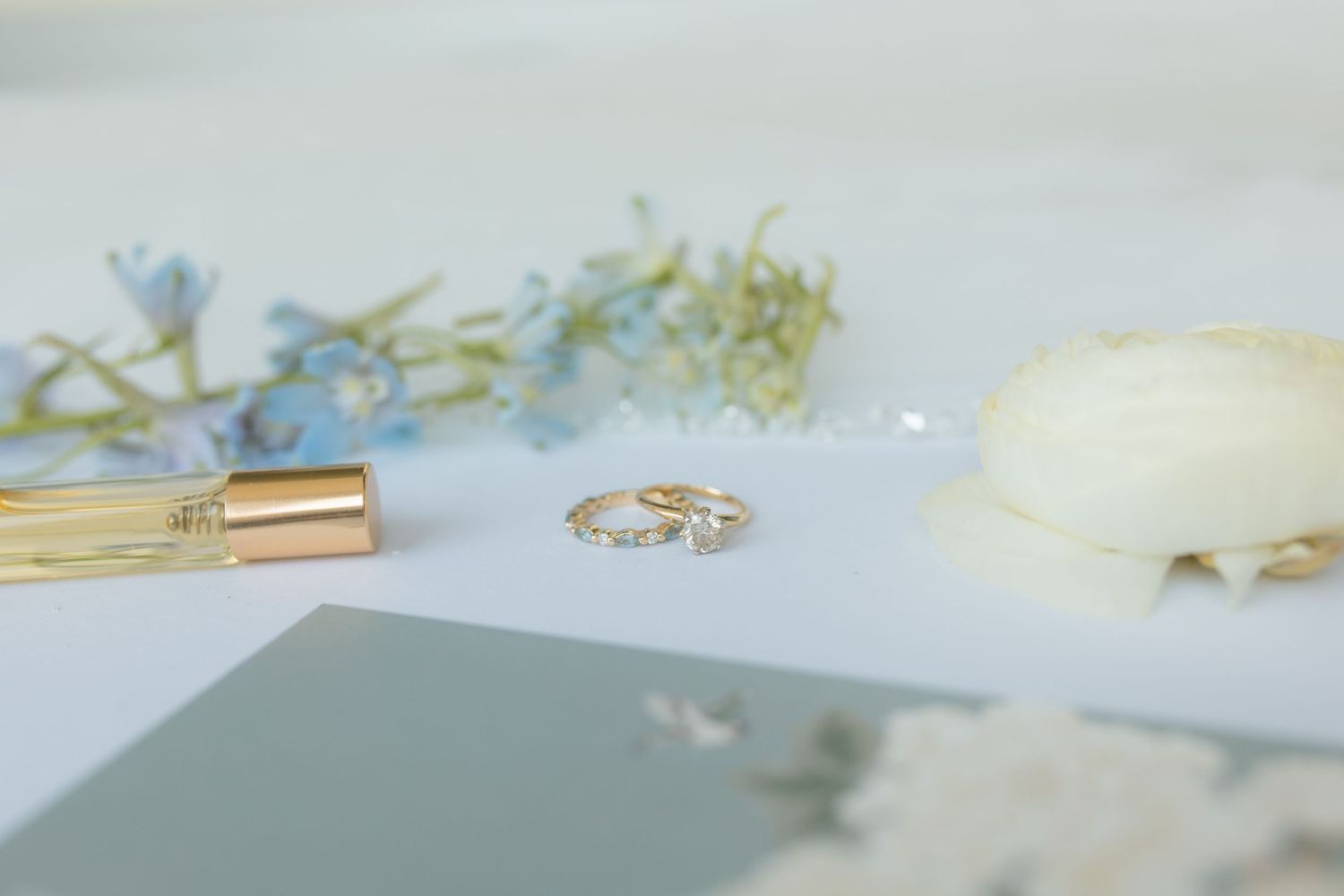 Delicate wedding details with a gold ring, blue flowers, and white candle arranged on a soft surface.
