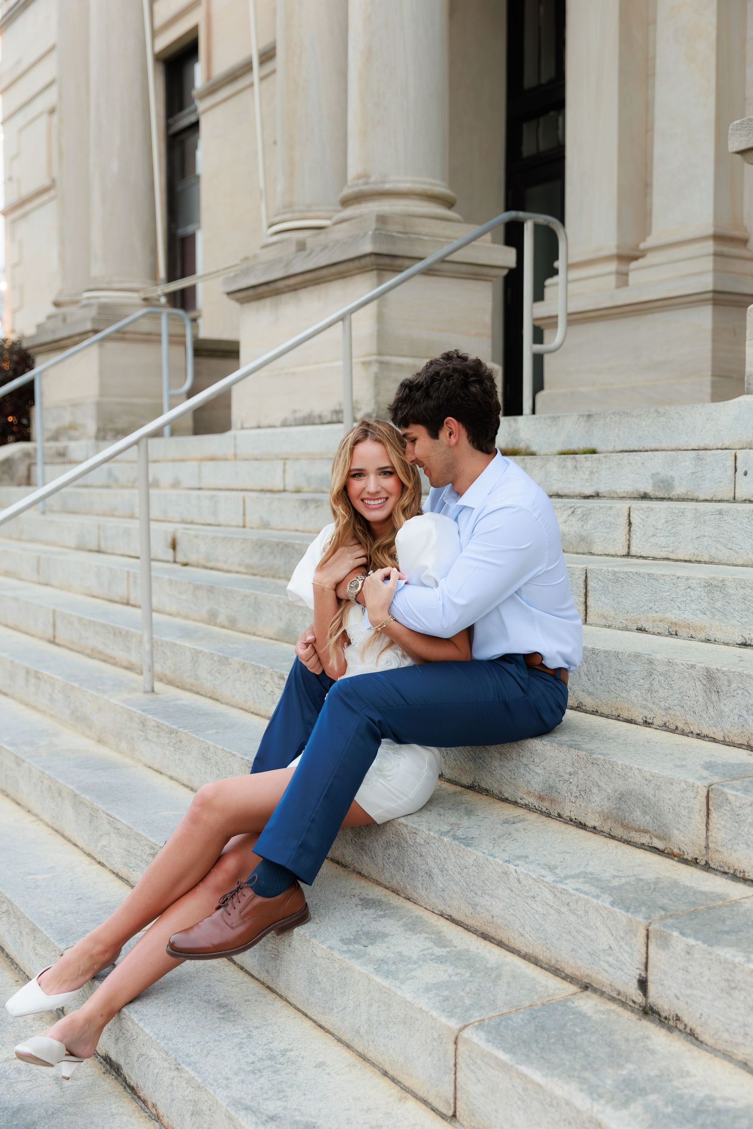 A couple lounges romantically on wide stone steps of an elegant building entrance.