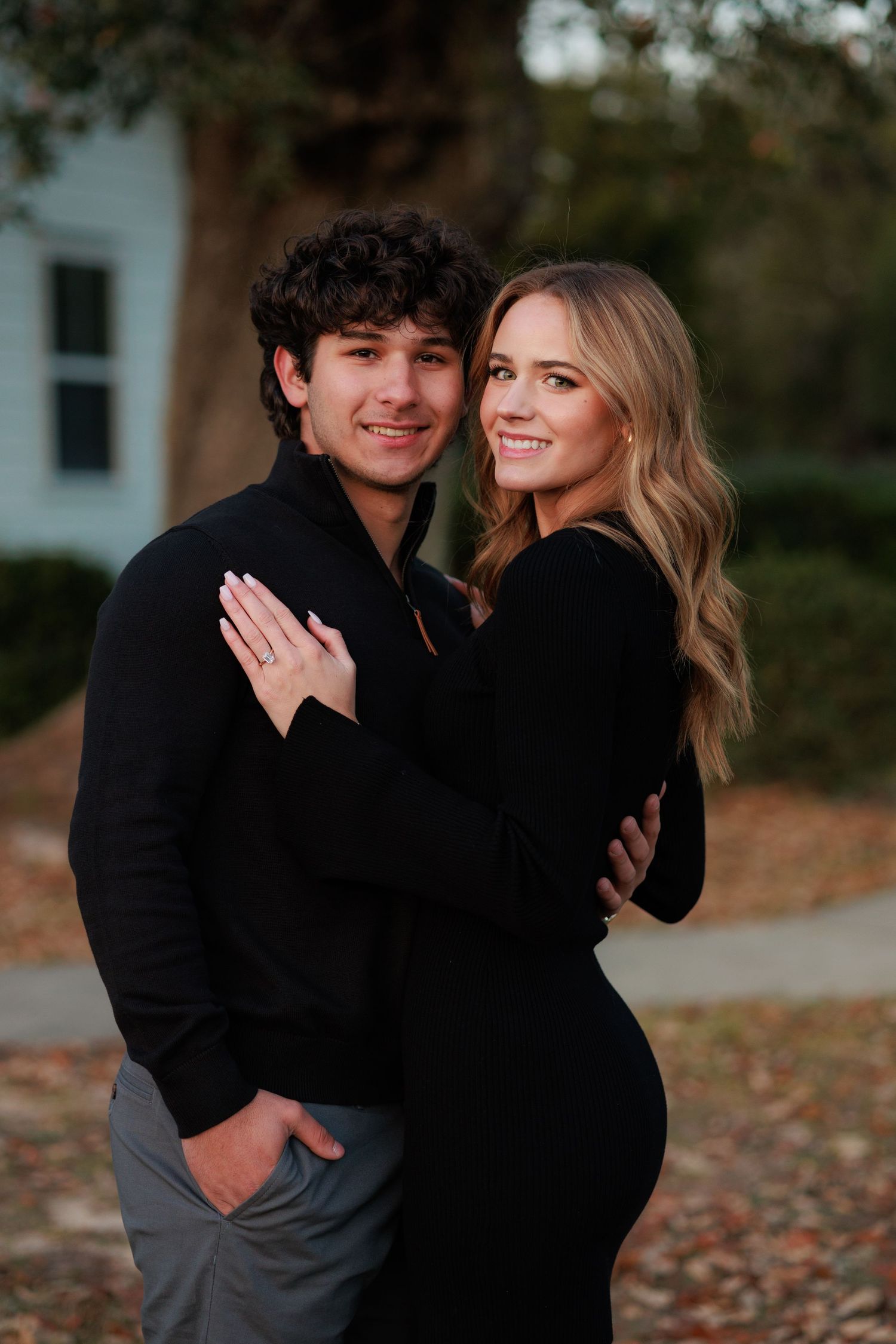 Couple in matching black outfits share romantic embrace during fall engagement photo session.