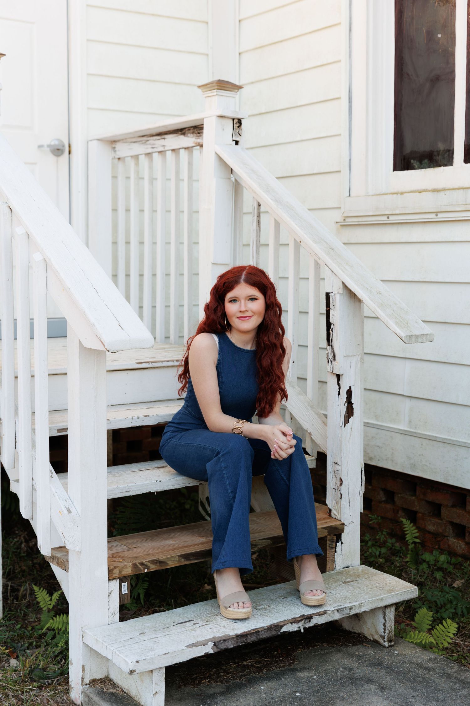 A person in jeans sits on white wooden porch steps in a casual outdoor setting.