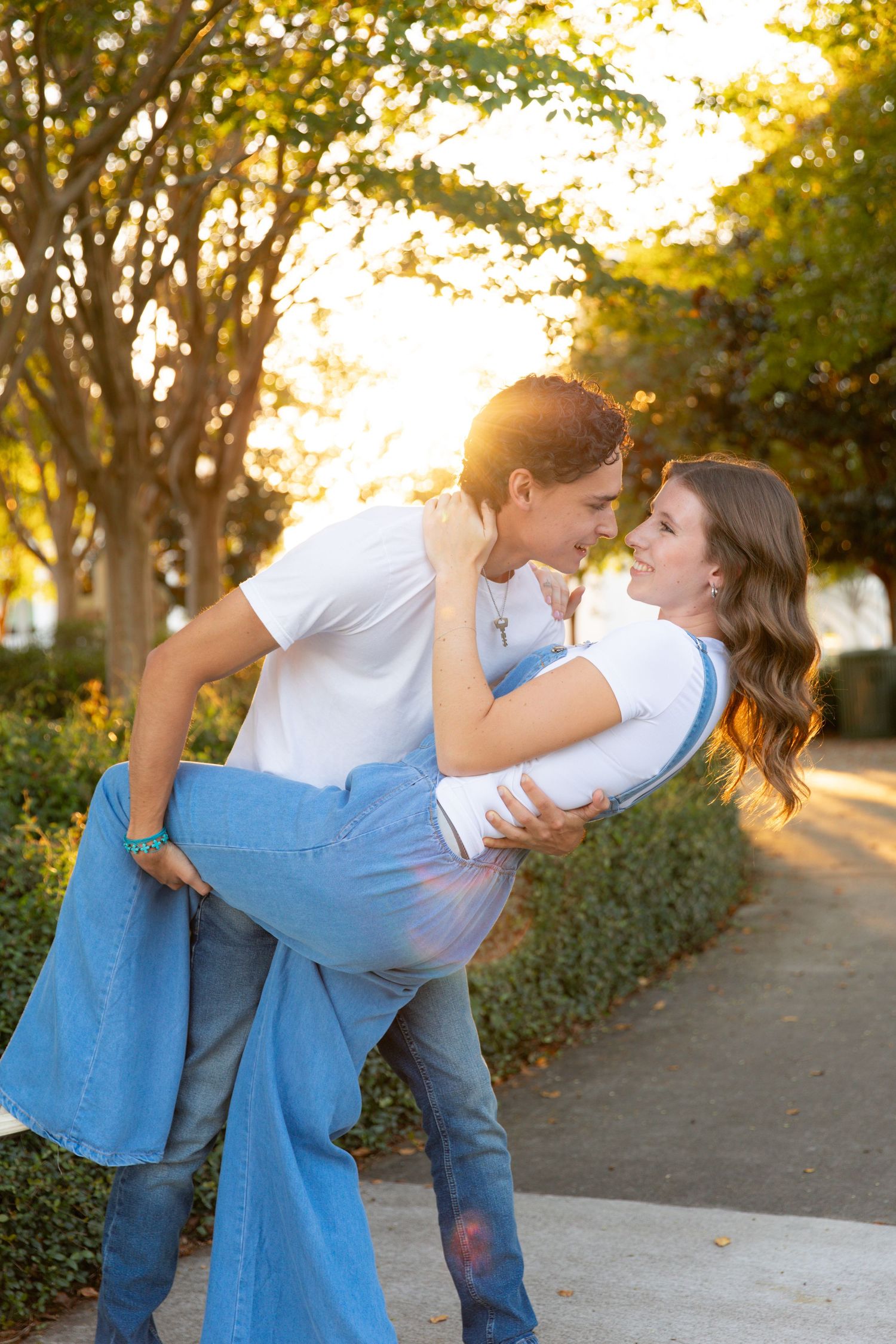 Romantic couple in casual wear sharing intimate moments during golden hour sunset in a park setting.