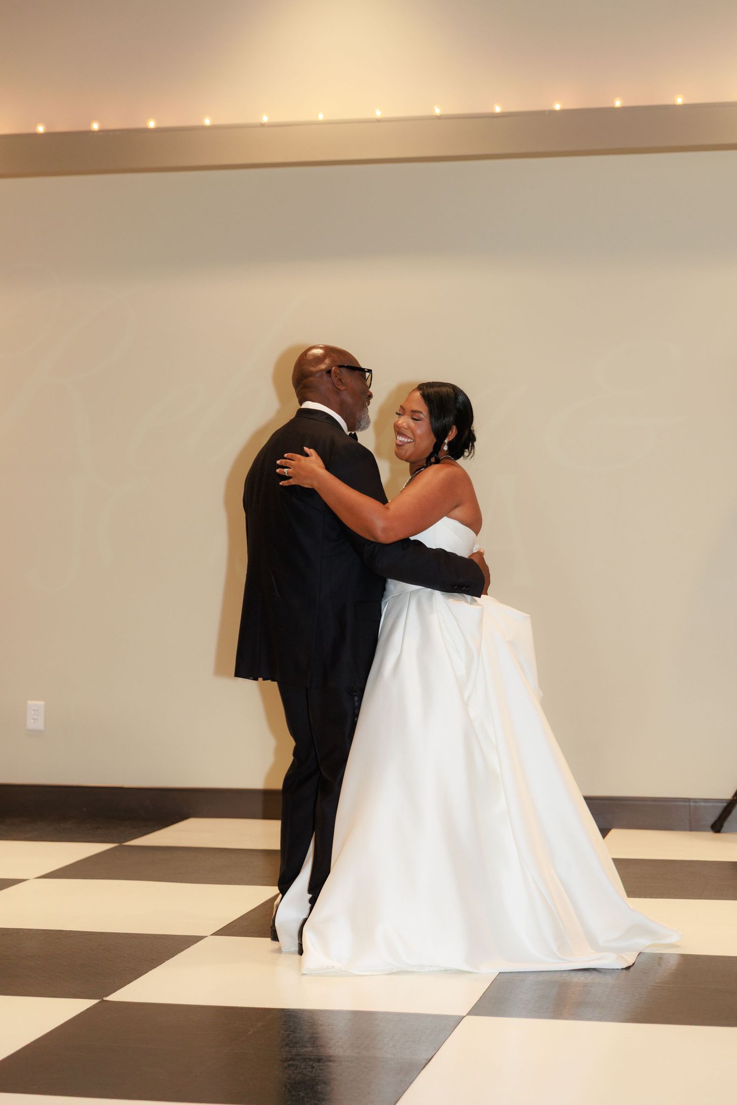 A couple dances together on a black and white checkered floor during a wedding celebration.