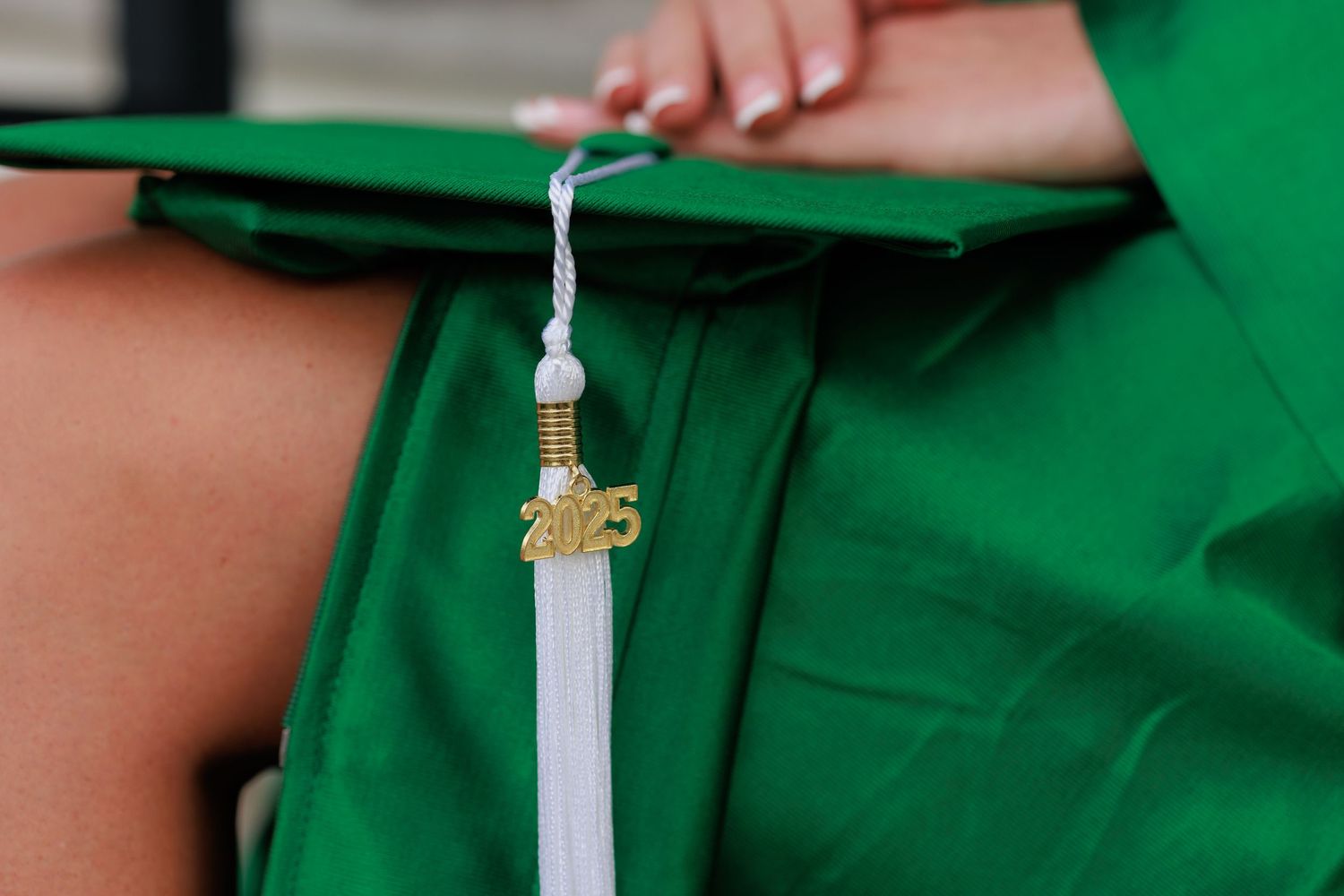 Close-up of a 2025 graduation cap tassel in gold and white on a green cap and gown.