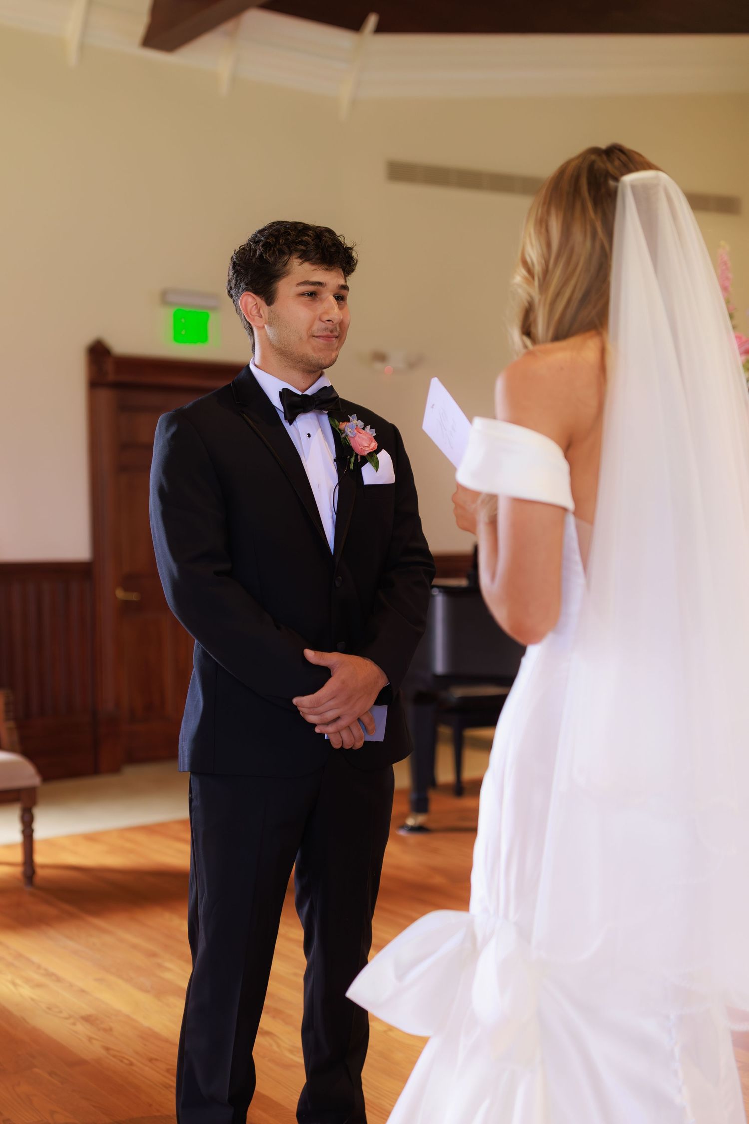 A couple exchanges wedding vows during their ceremony, with the groom in a black tuxedo and the bride in a white dress and veil.