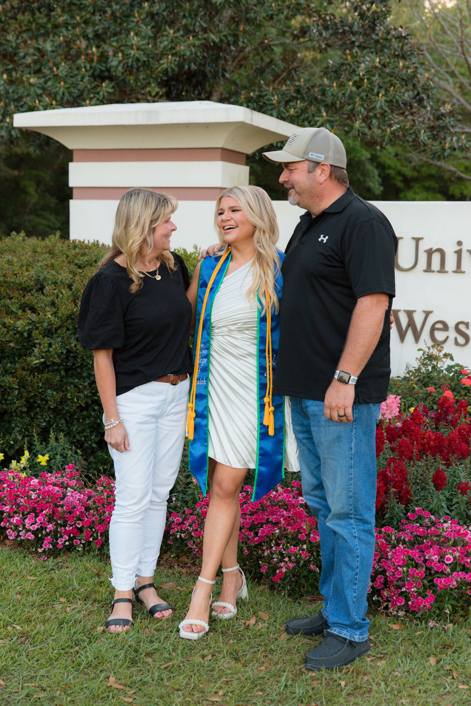 People standing together by vibrant pink flowers and white building in an outdoor garden setting.