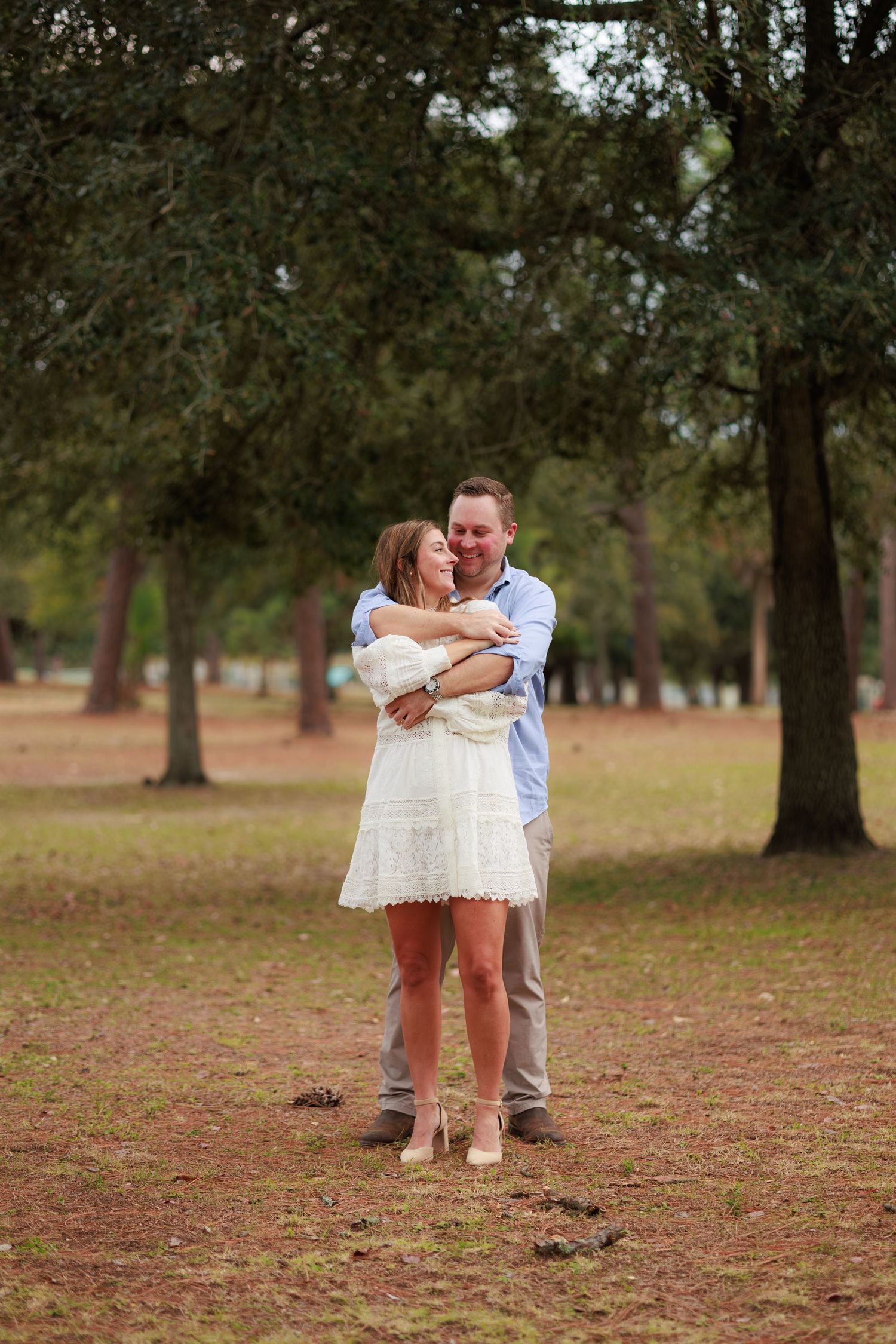 A couple shares a romantic moment together in a park setting with scattered autumn leaves on the ground.