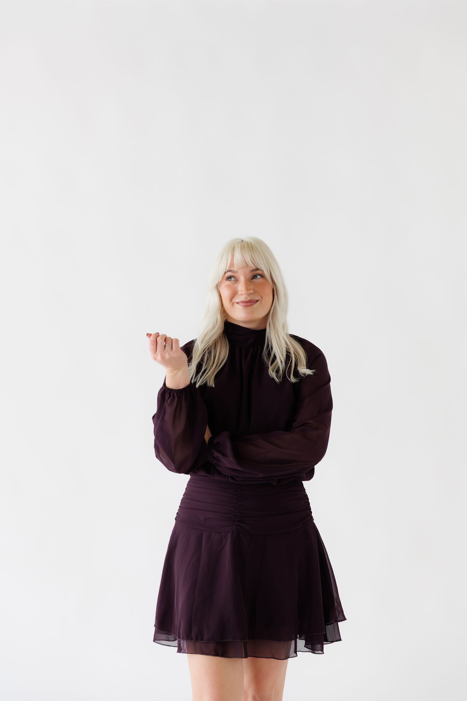 A person in a dark purple sweater dress and boots poses against a white backdrop.