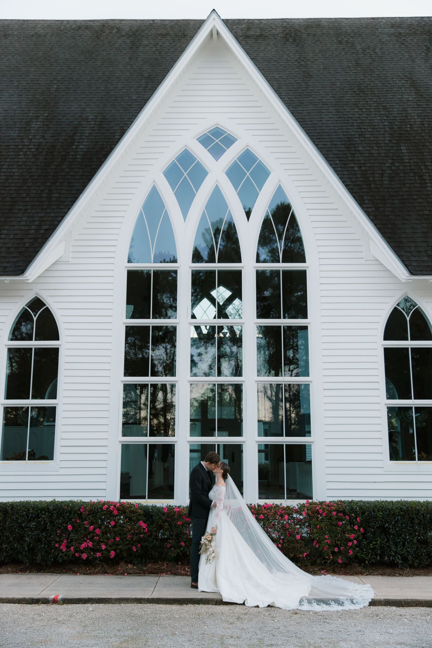 White chapel with Gothic arched windows and trailing bridal veil creates elegant wedding backdrop.