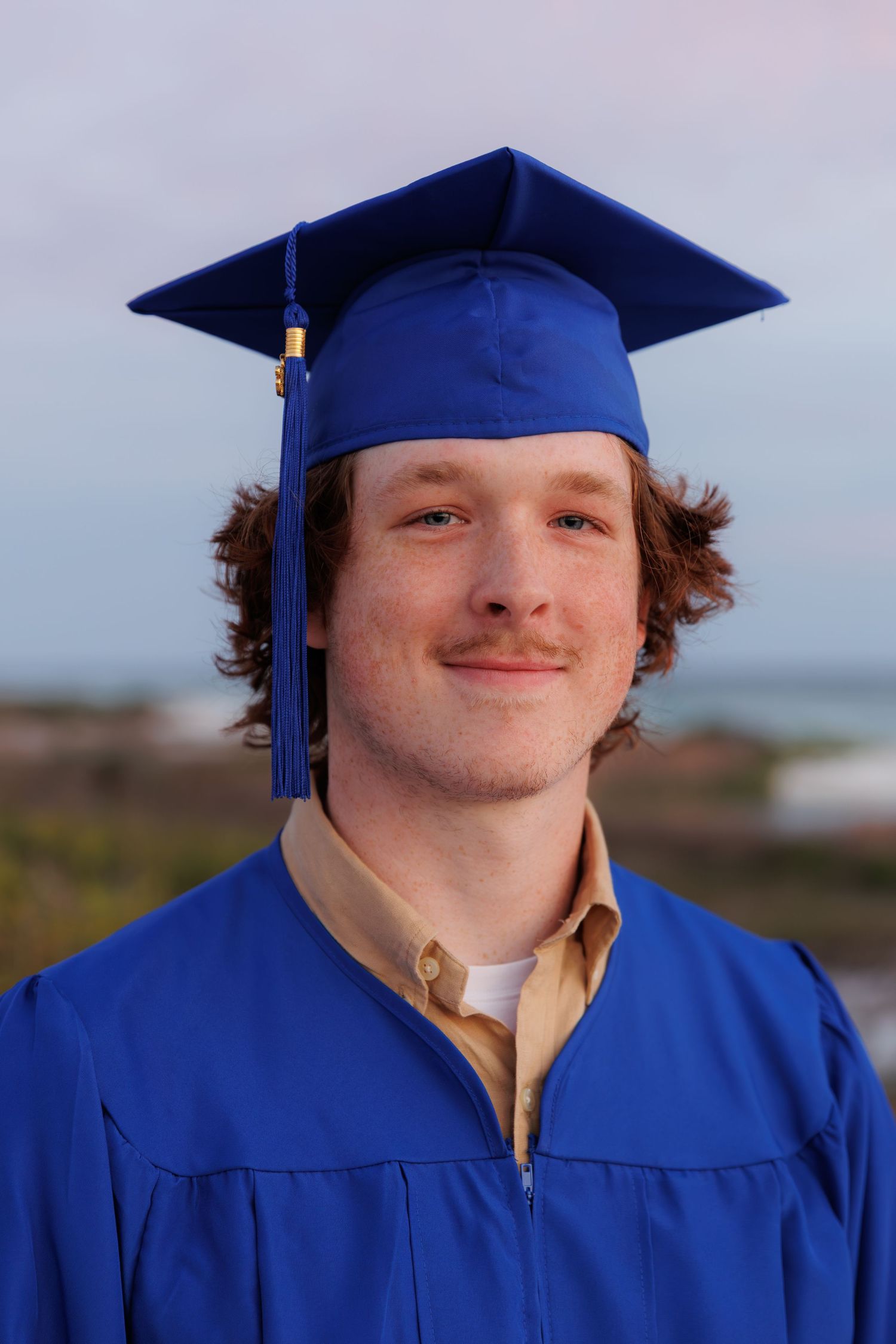 Close-up portrait of young male graduate in blue cap and gown outdoors.