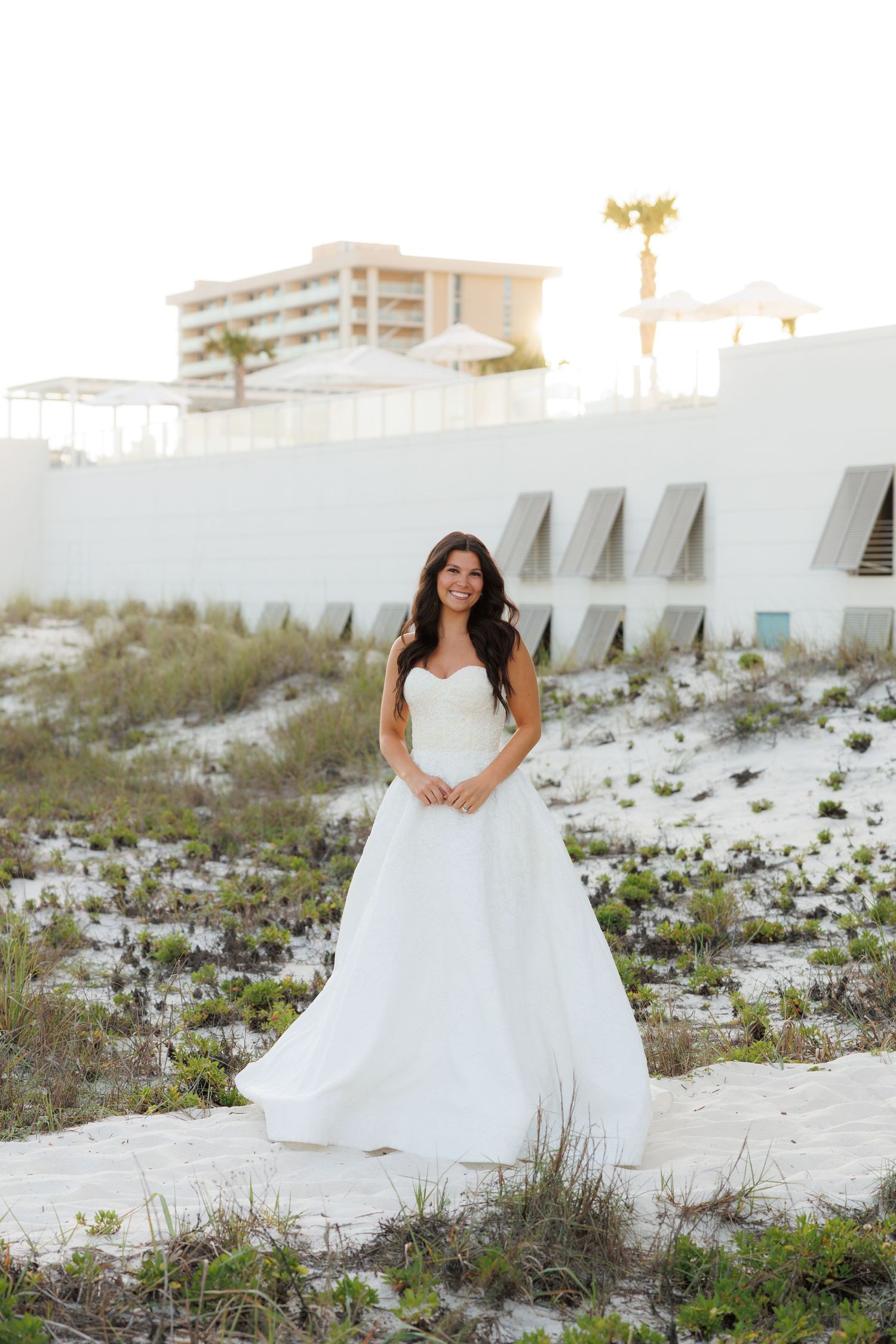 Radiant bride in strapless white gown poses on sandy beach dunes.