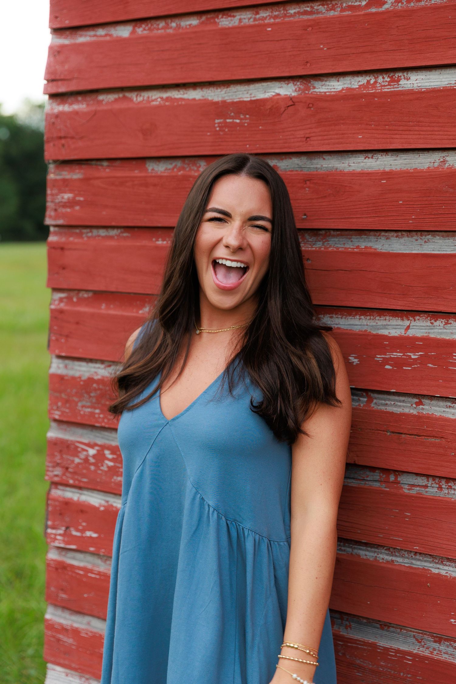 Joyful woman in blue dress laughing against weathered red barn siding.