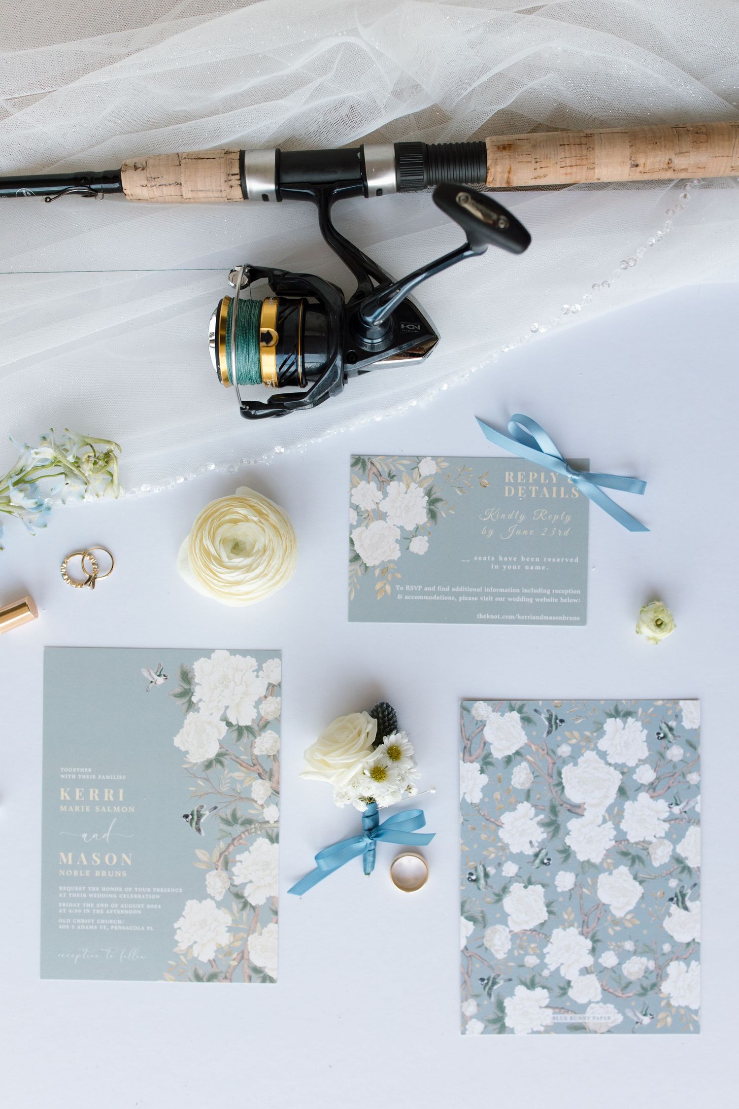 Elegant wedding invitation suite in blue and white floral design with a fishing rod displayed above.