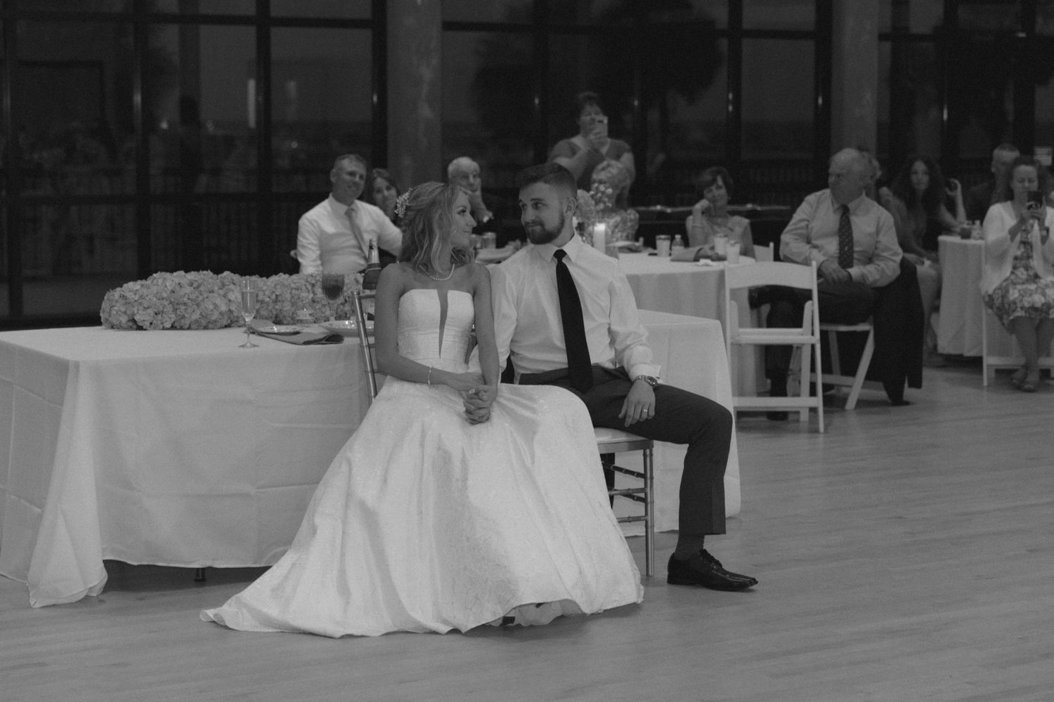 Black and white photo of newlyweds sitting together during their wedding reception.